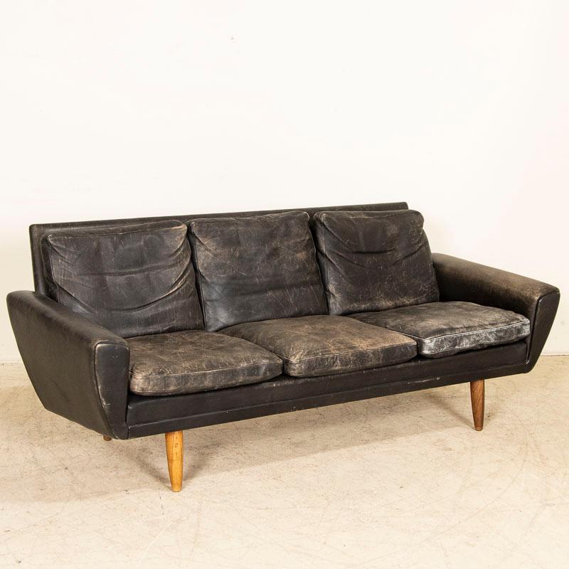This handsome mid-century design sofa was made in Denmark, circa 1960 showing off timeless style in its lines and curves while resting on four cylindrical wood feet. The six cushions are removable and reflext years of wear as the black has faded and