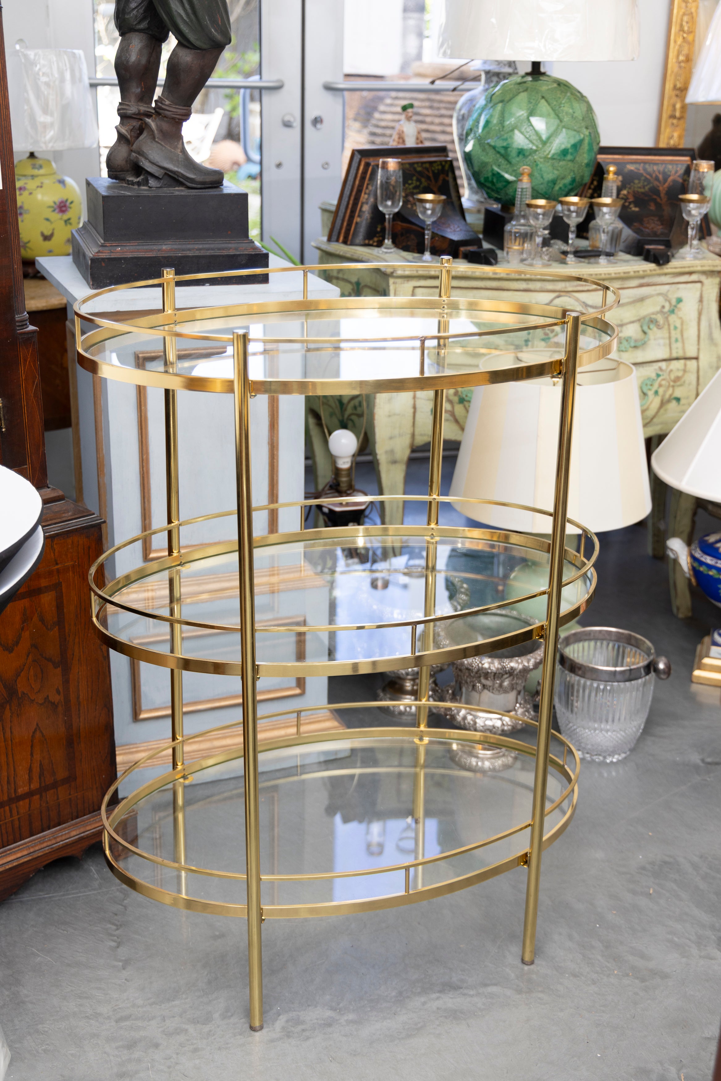 Si tratta di un bel mobile bar ovale in ottone della metà del XX secolo con tre livelli di ripiani in vetro, incorniciati da gallerie in ottone.  Il carrello è dotato di rotelle per garantire la mobilità.