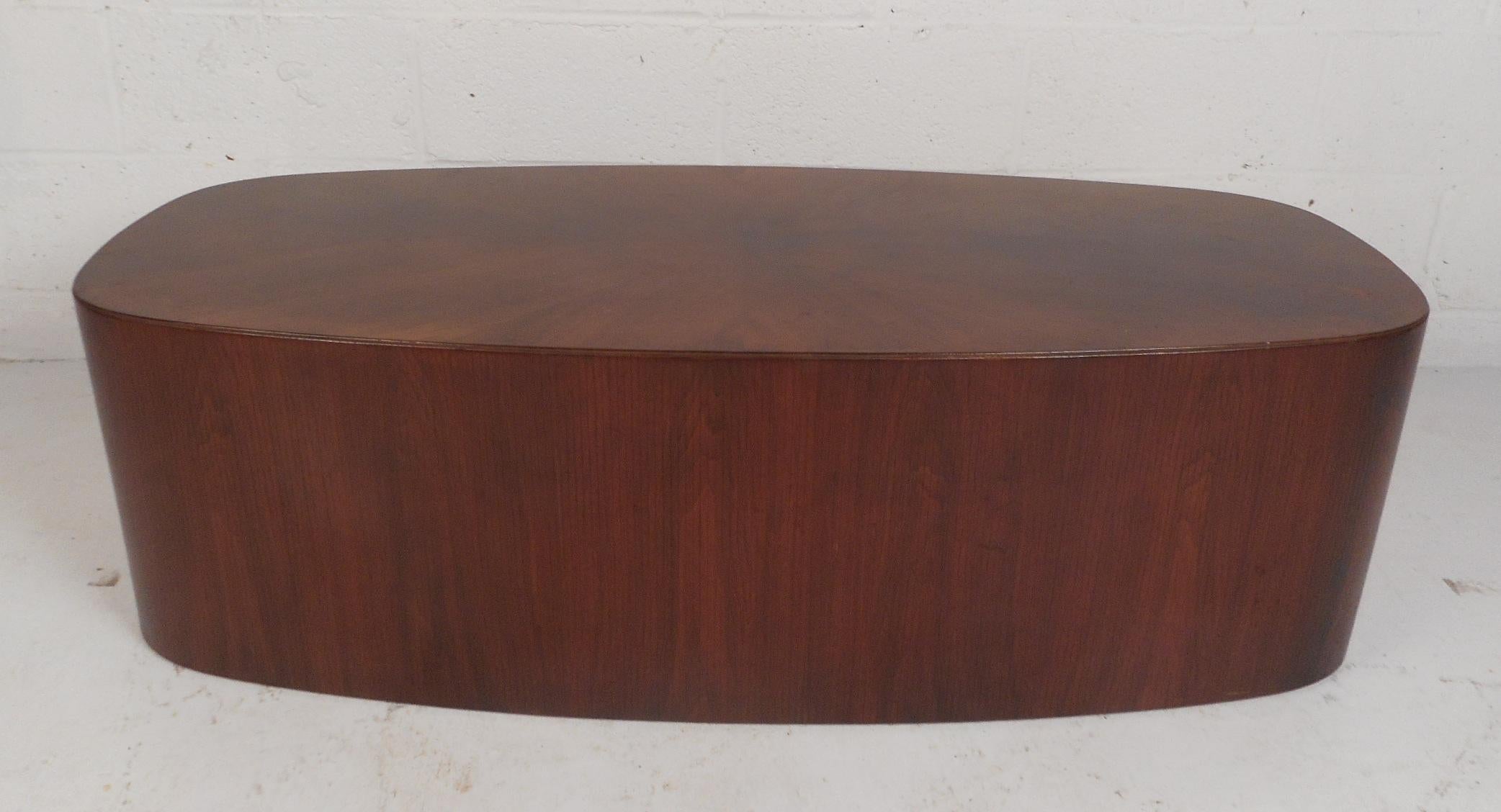 This beautiful vintage modern coffee table features unique wood grain on the top running in different directions. An oval shape, smooth edges, and a wonderful dark walnut finish adds to the allure. This stunning coffee table makes the perfect