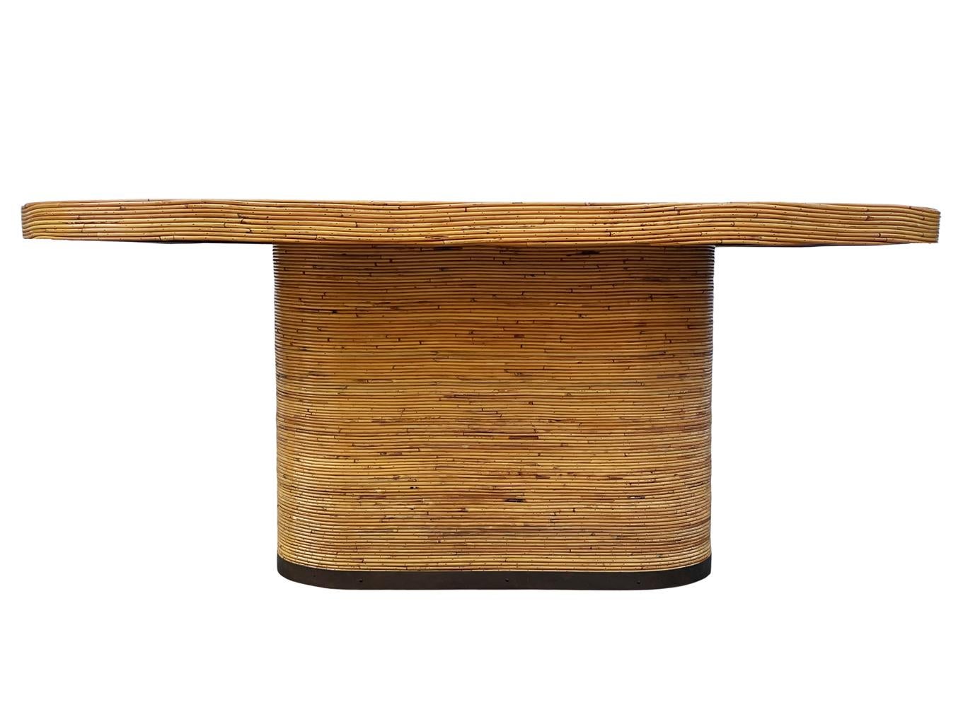 Une grande et impressionnante table à manger, datant des années 1950. Le plateau de la table a la forme d'un ovale de piste de course et est enveloppé de roseaux de crayon cloués. Le plateau a une plaque de laiton incrustée et la basse est en bronze