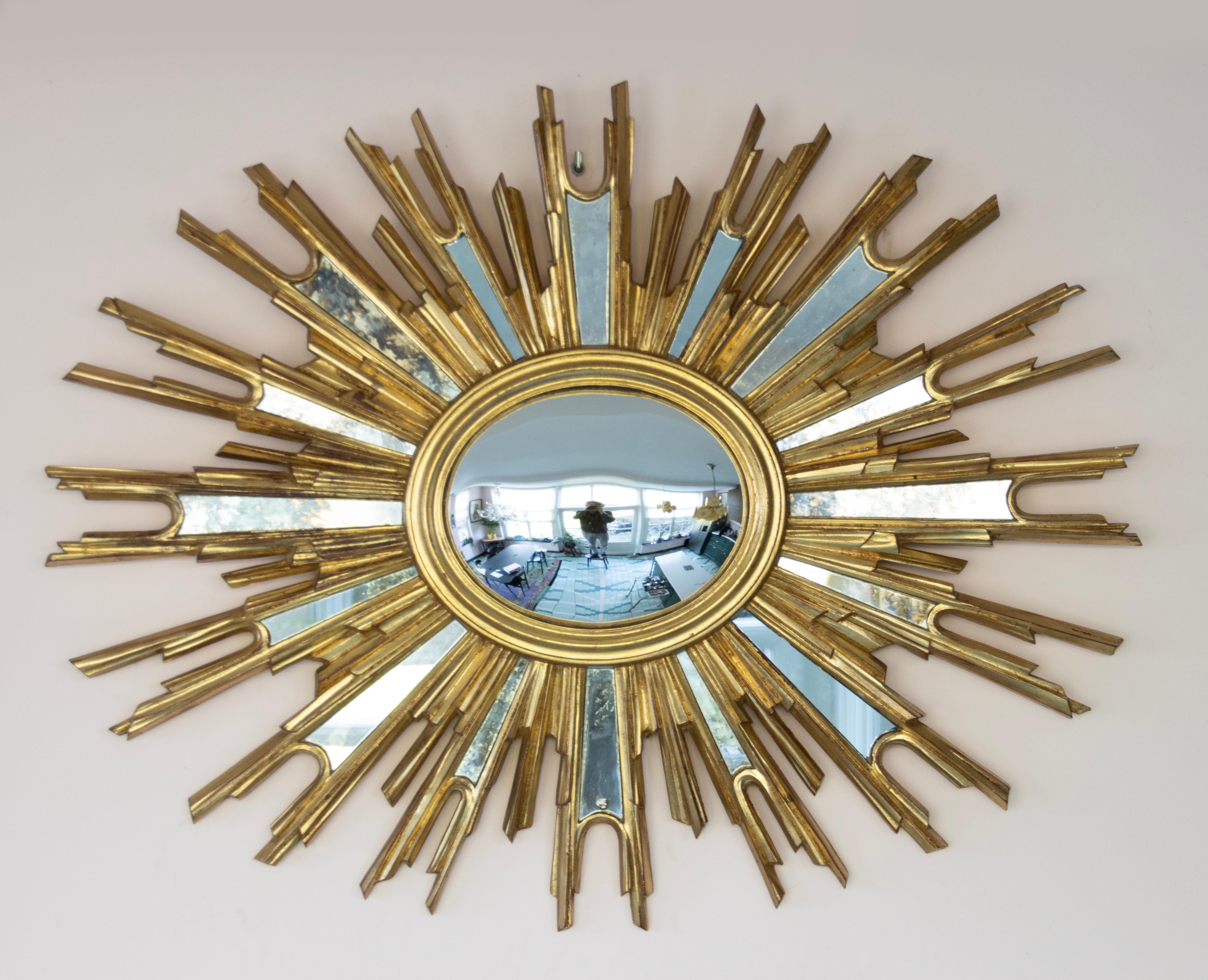 A mid-century modern large gilded sunburst convex mirror with small mirror glasses in the sun rays. In the center a curved convex mirror. The mirror can be hung in two ways, horizontal and vertical. The mirror is made of resin. 
Made in Belgium,