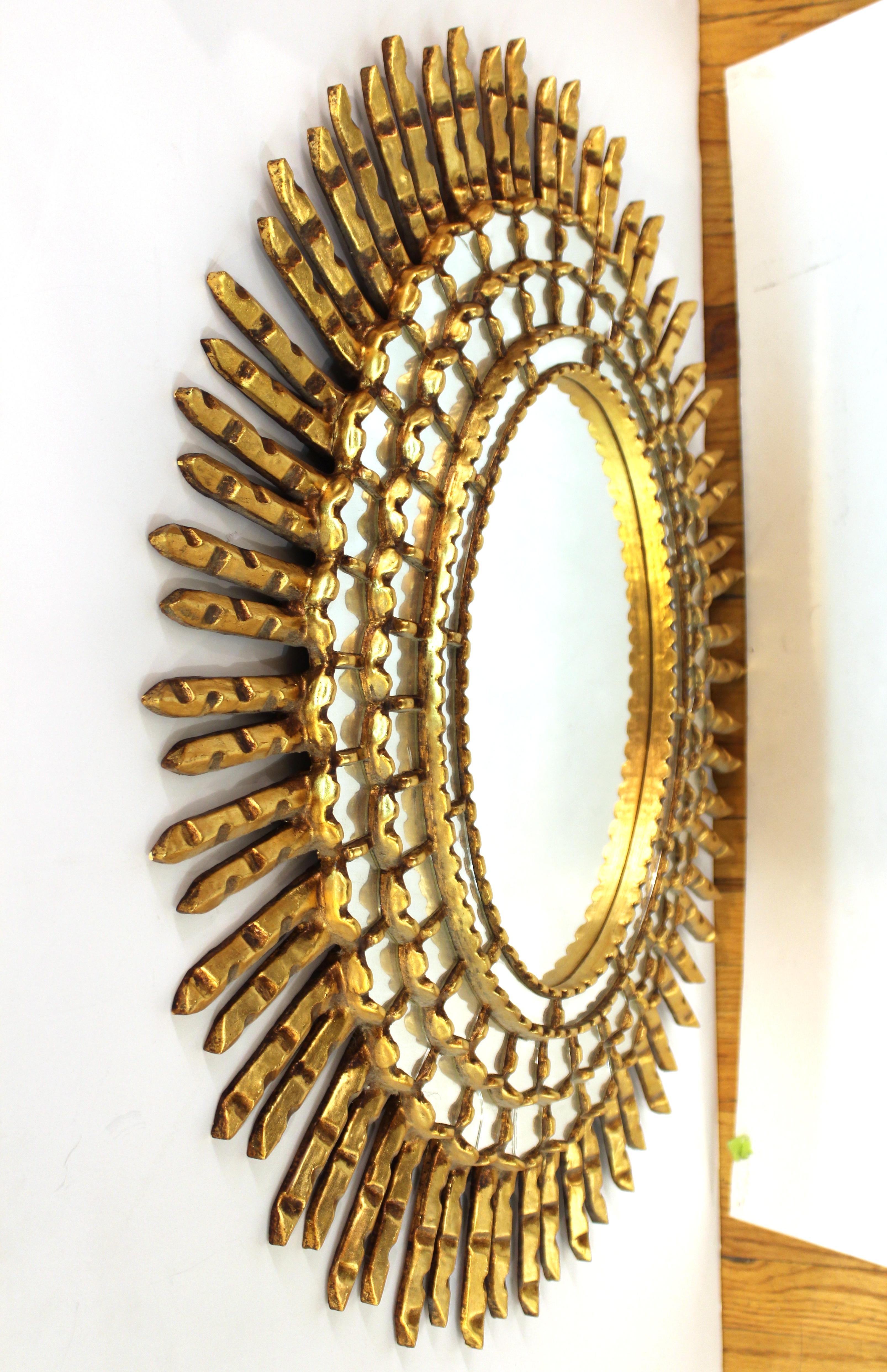Mid-Century Modern oval shaped sunburst wall mirror. The piece is made of giltwood with inserted concentric circles of mirrored elements and wooden rays. In great vintage condition with age-appropriate wear and some minor cracks in the smaller