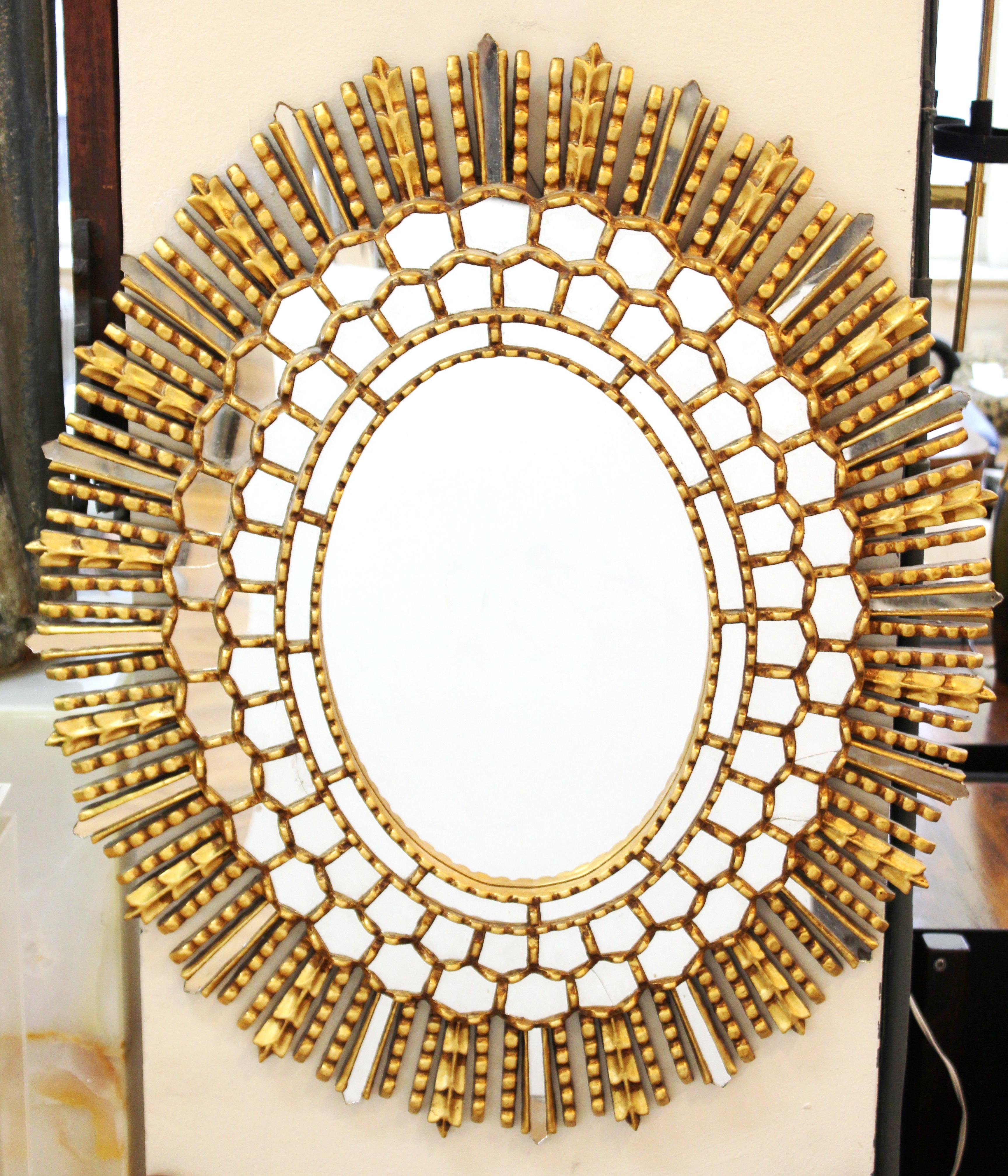 Mid-Century Modern oval shaped sunburst wall mirror. The piece is made of giltwood with inserted concentric circles of mirrored elements and wooden rays intermixed with mirrored rays. In great vintage condition with age-appropriate wear and some