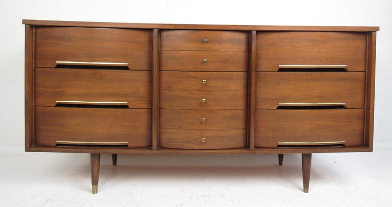 Great pair of matching midcentury low and highboy dressers in walnut. Featuring gently bowed fronts with a subtle metal accent trim, dovetail drawer construction and tapered brass-capped legs, this dresser combo provides ample storage space and