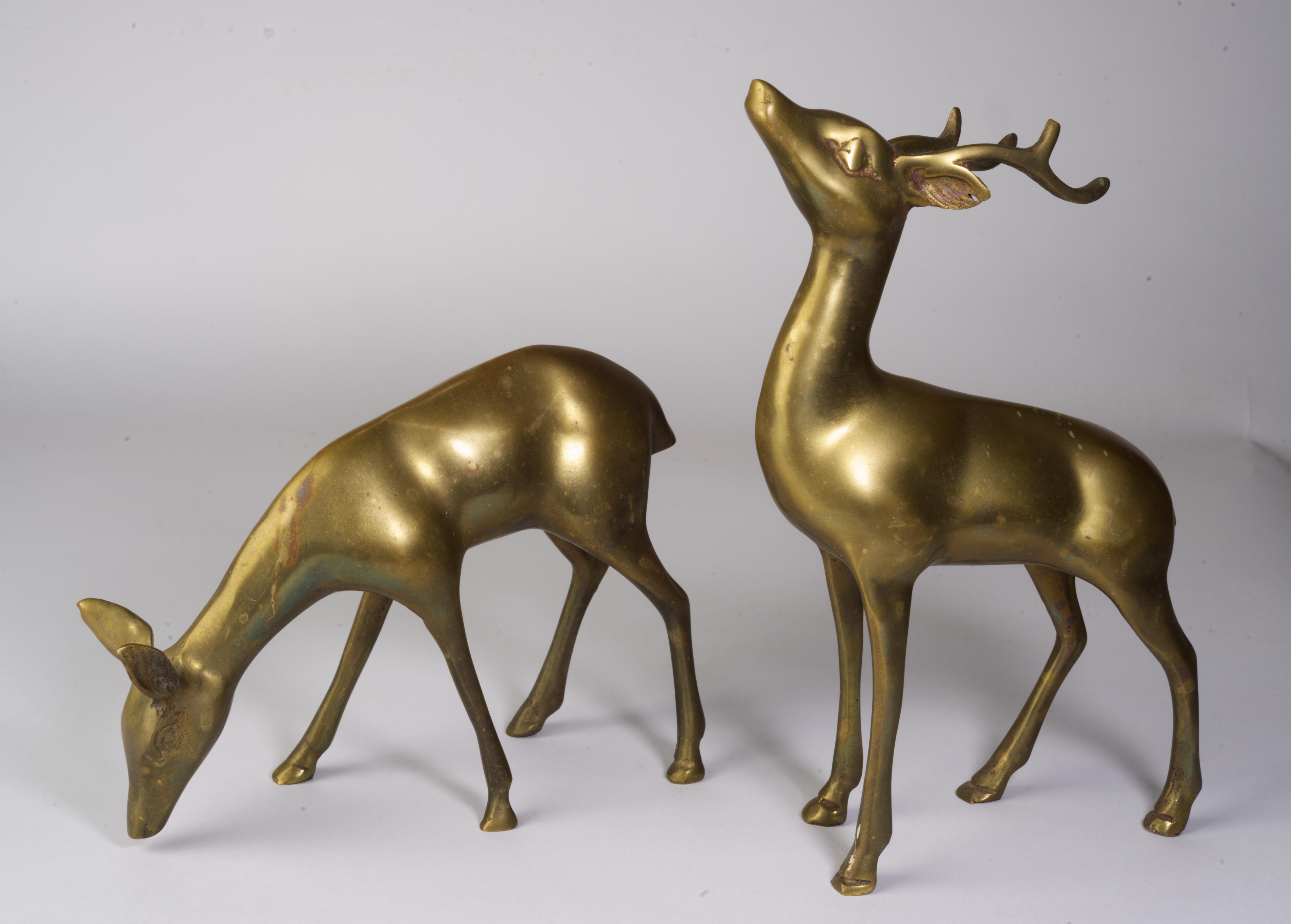  Mid-Century Modern pair of bronze deer consists of one buck and one doe, with the buck standing upright displaying his antlers and the doe grazing on the ground. 

The brass has nice patina consistent with age.