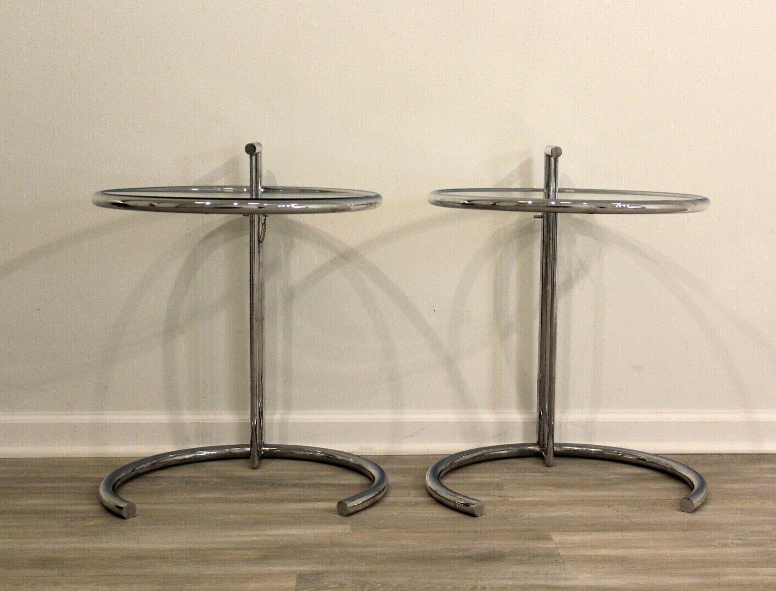A pair of Eileen Gray style chrome and glass adjustable side end tables. In excellent condition. Dimensions: 20 diameter x 25height/32height.
 