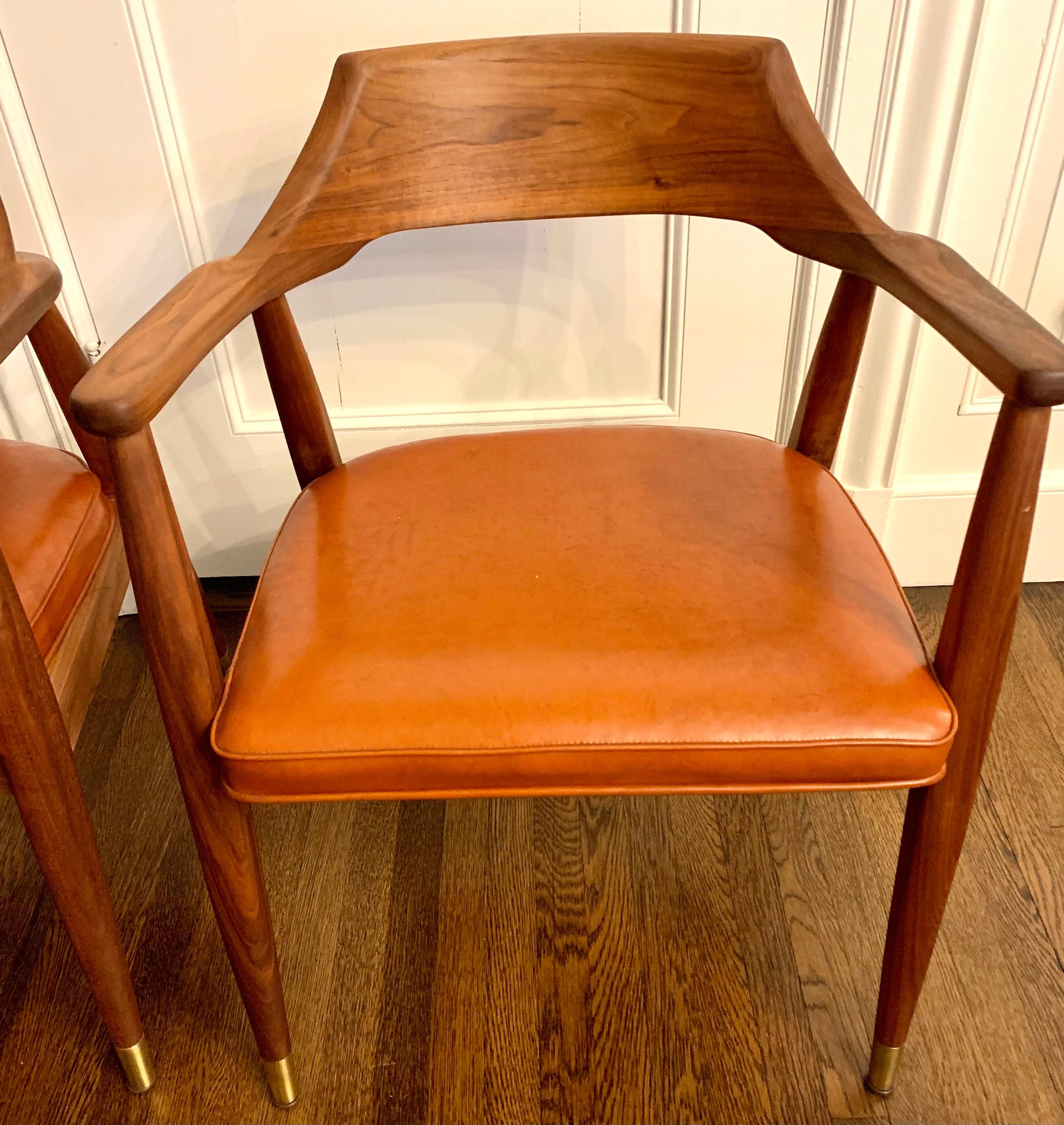 Pair of vintage mid century curved back arm chairs with solid walnut frame and original orange leather upholstery. Manufactured by the Jasper Chair Co., Jasper, Indiana - founded 1921. Scandinavian inspired design with curved back rests angled legs