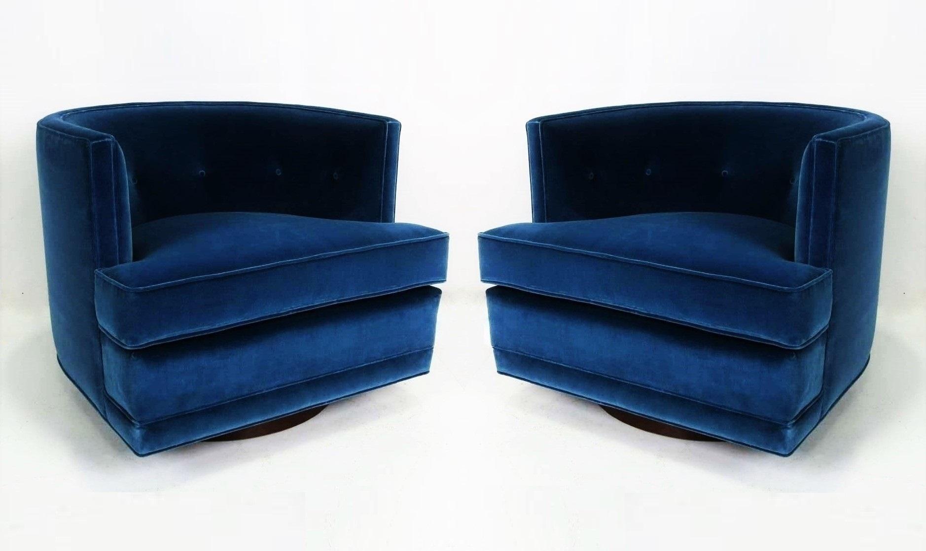 Luxurious pair of swivel lounge chairs freshly upholstered in a blue velvet. Attributed to Harvey Probber. They feature a barreled tufted back, oversized detached cushion seat and flat front aprons. All sit upon round walnut swivel bases, freshly