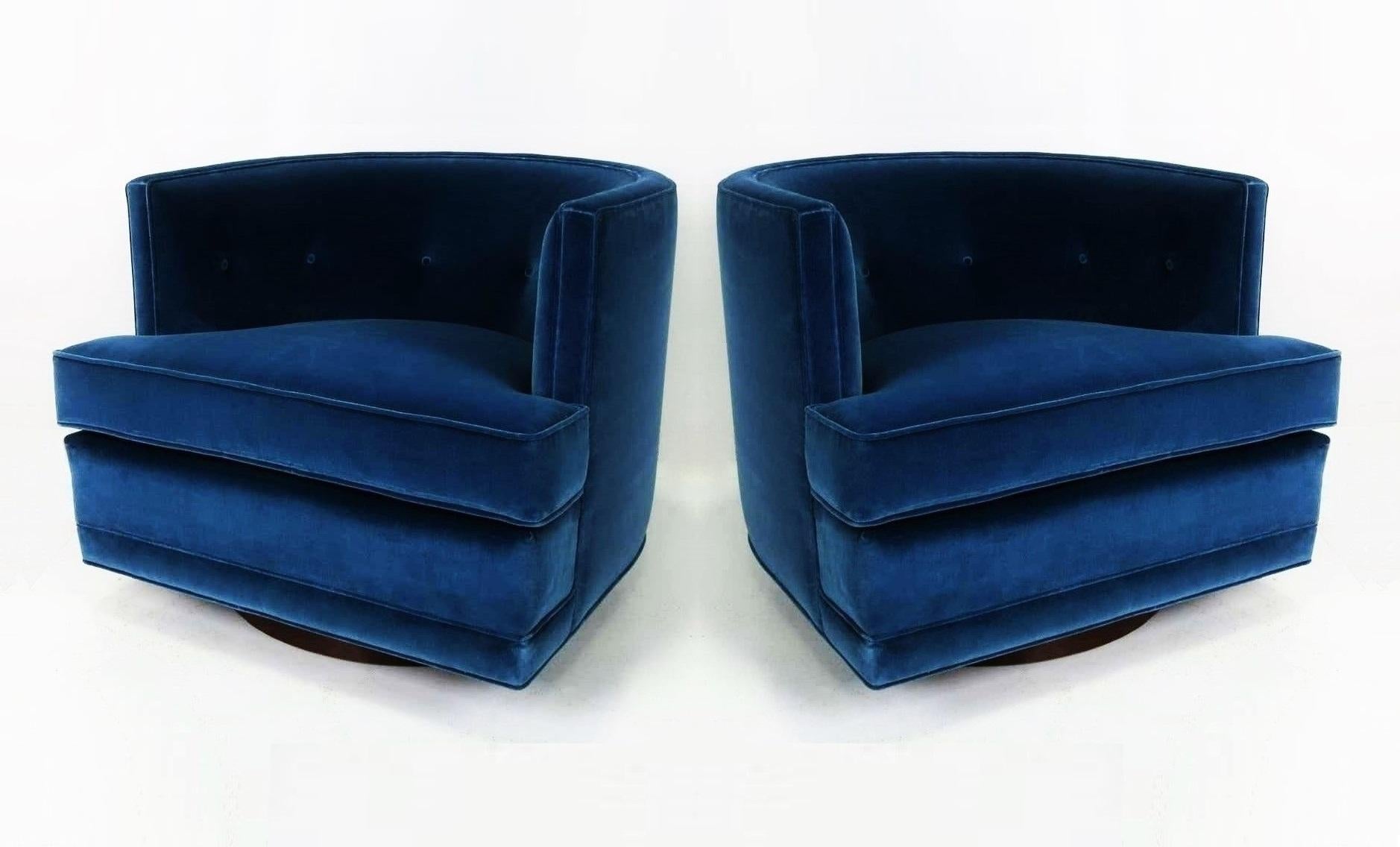 Luxurious pair of swivel lounge chairs freshly upholstered in a blue velvet. Attributed to Harvey Probber. They feature a barreled tufted back, oversized detached cushion seat and flat front aprons. All sit upon round walnut swivel bases, freshly