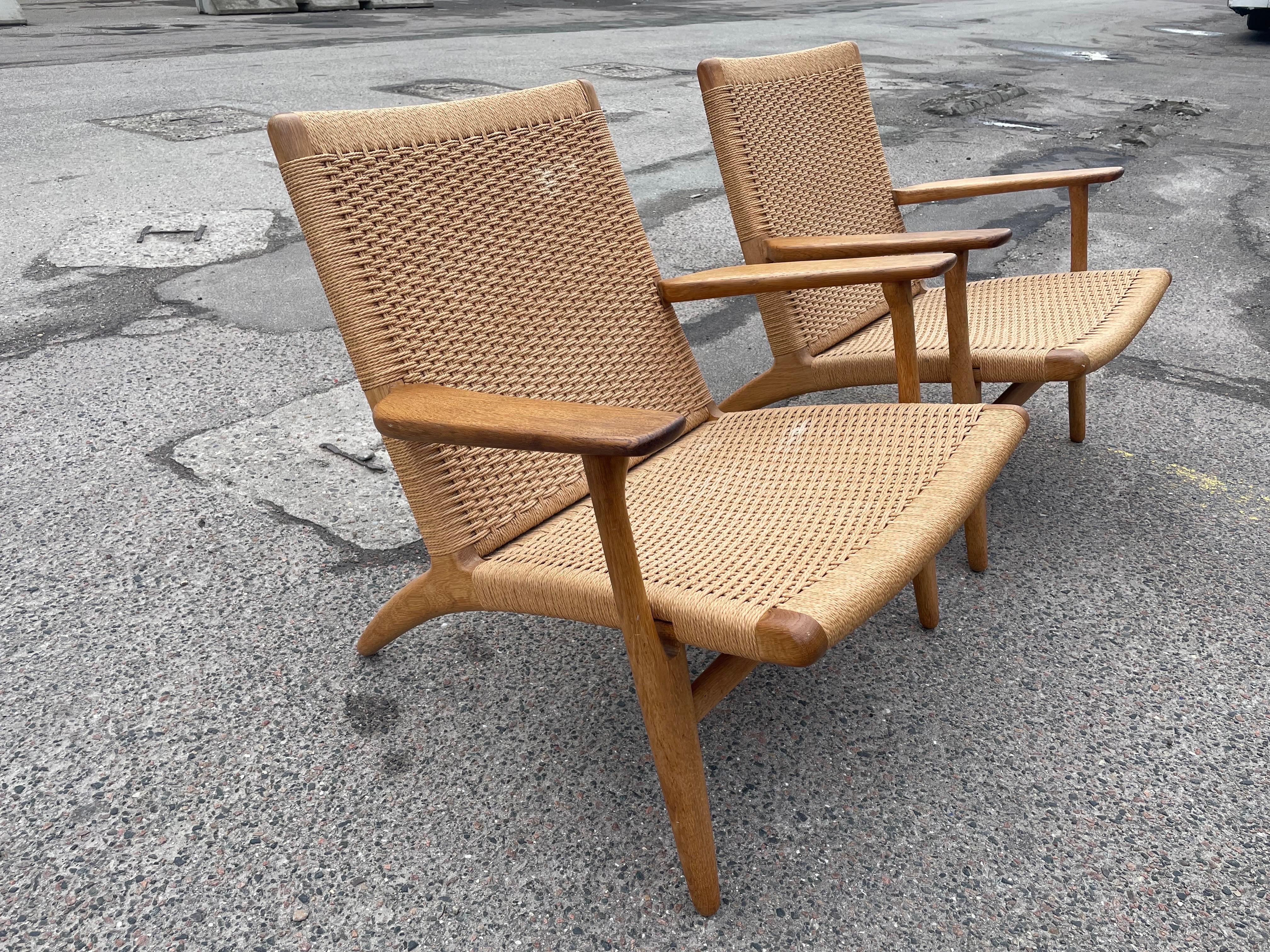 Introducing a rare opportunity to own a true piece of design history - a pair of CH25 lounge chairs by renowned Danish designer, Hans Wegner. These chairs are the epitome of Mid-Century Modern design, and are highly sought after by collectors and