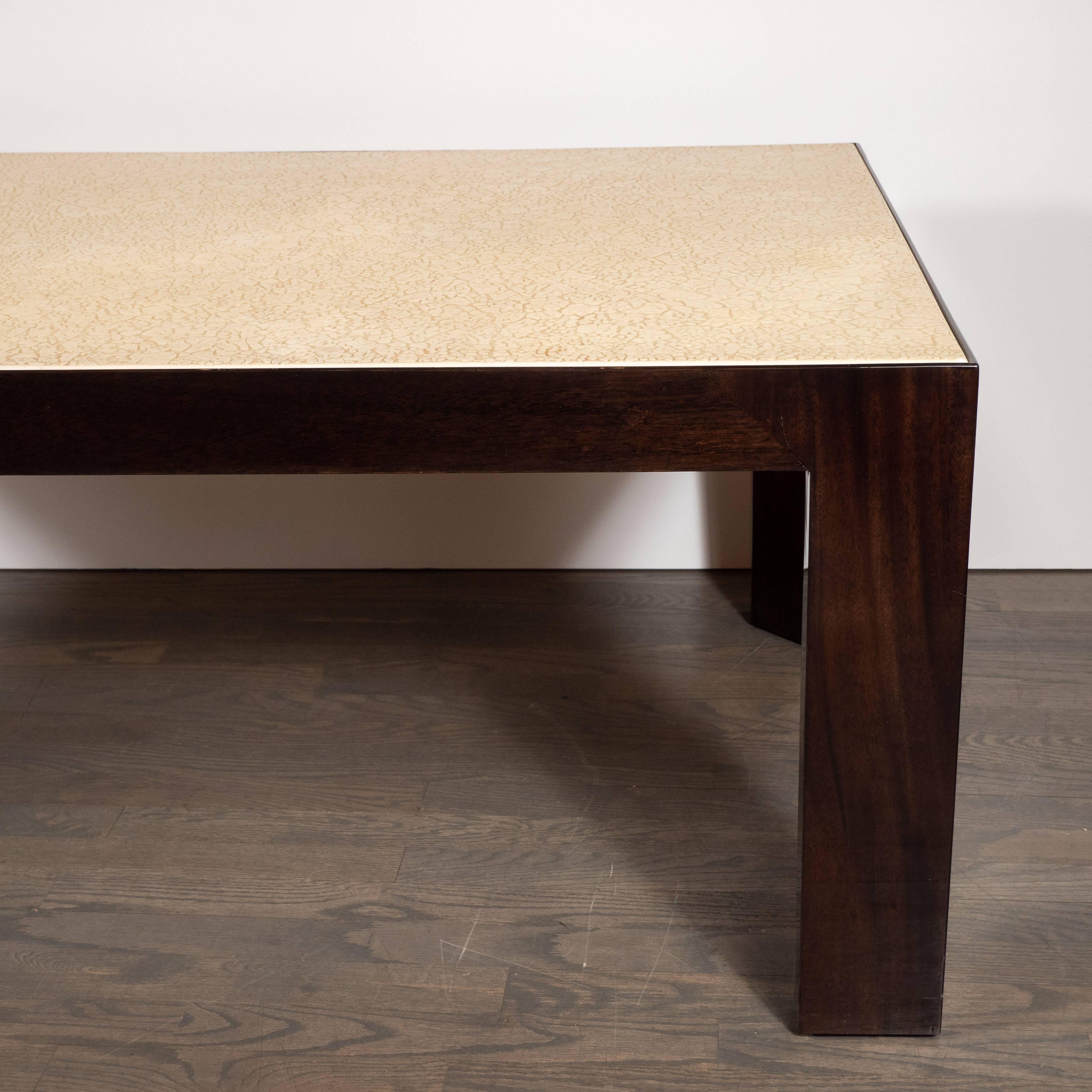 This sophisticated cocktail table was realized in the United States, circa 1980. It features a Parson style body with rectangular legs and apron composed of hand rubbed walnut, as well as a resin craqueleur top. The top, executed in a cream hue,