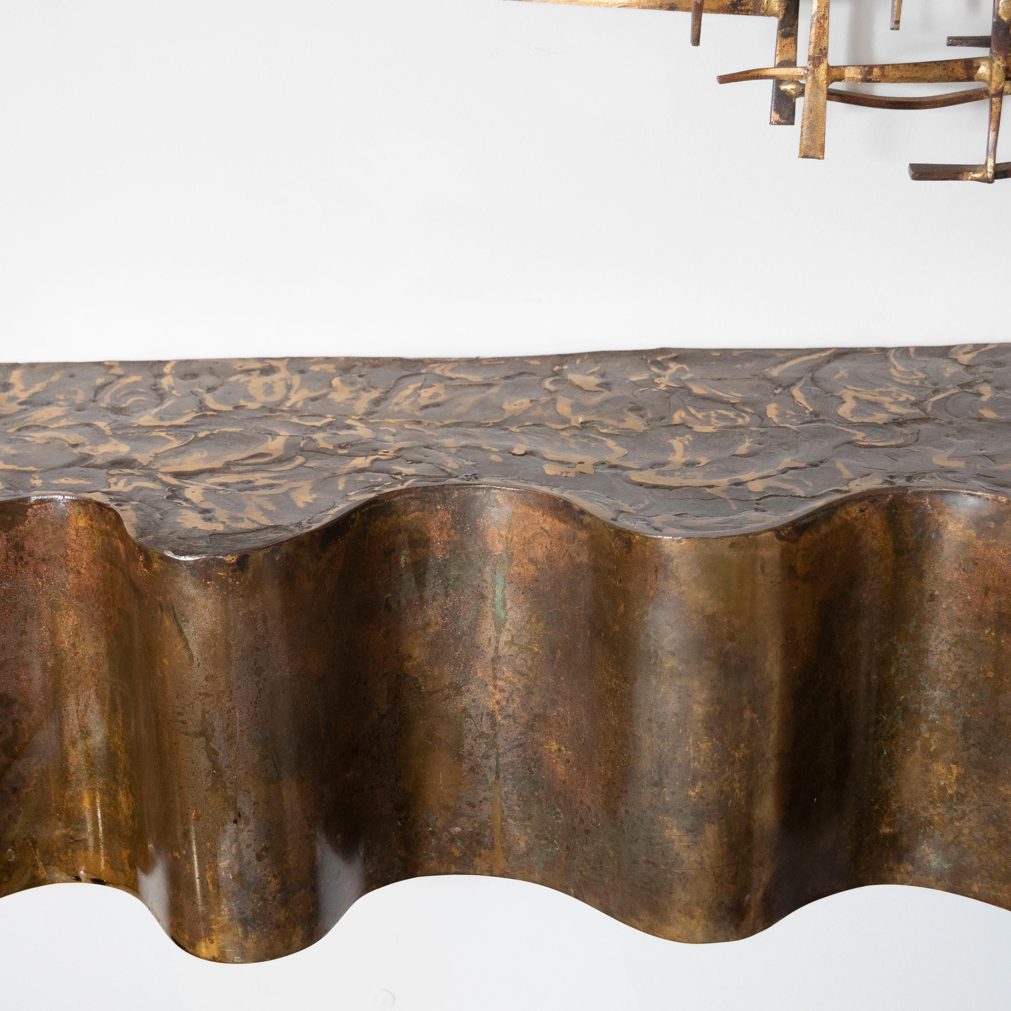 This sophisticated Brutalist console shelf was realized, in the manner of Paul Evans, in the United States, circa 1970. It features an undulating wave front in sculpted bronze with an expressionistically patinated top. With its refined aesthetic and