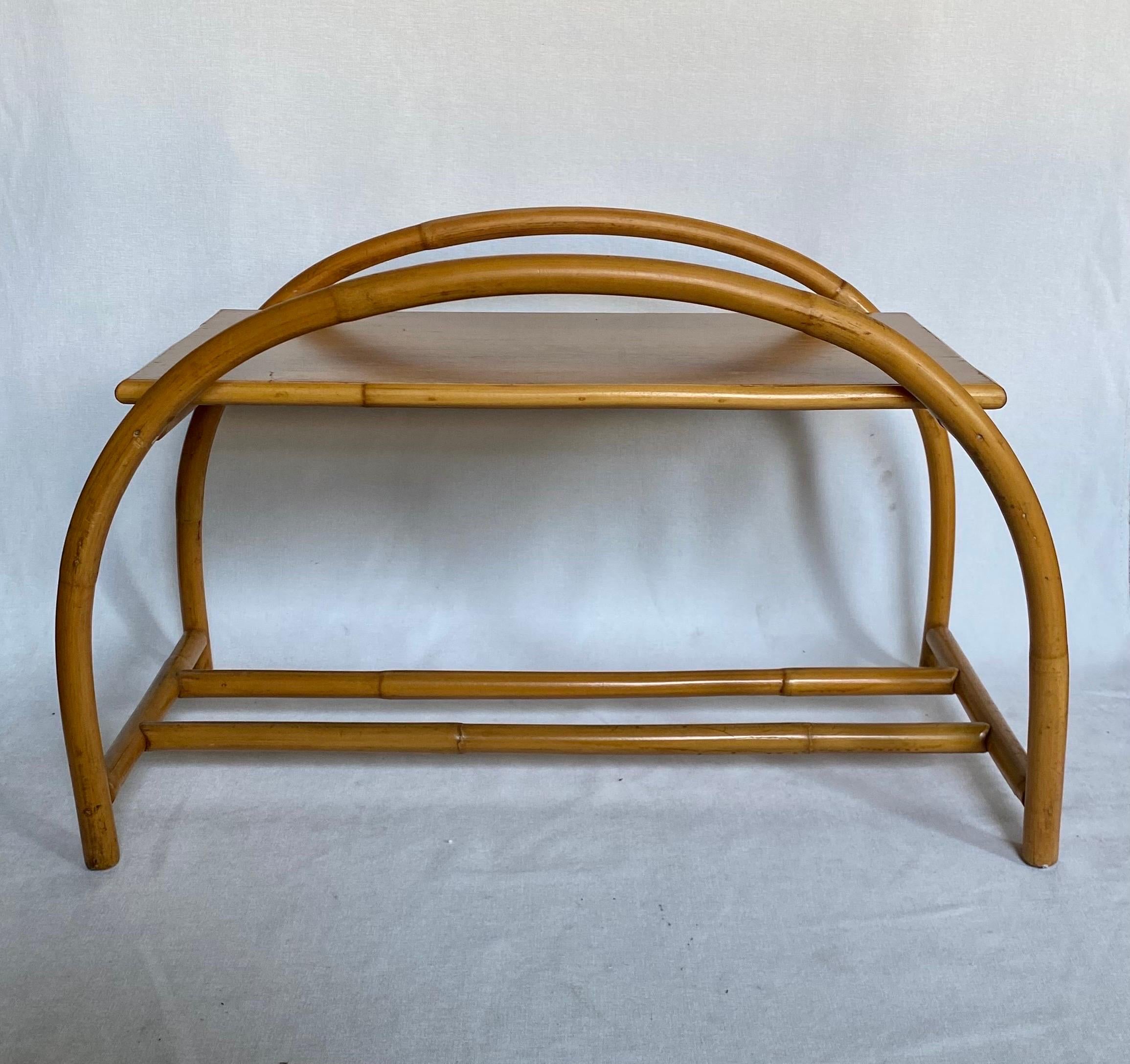 Sculptural Mid-Century Modern natural rattan side or end table with removable clear glass top. This Palm Regency style accent table features a curved arch design with a double stretcher base and natural wood top. In the style of Paul Frankl.