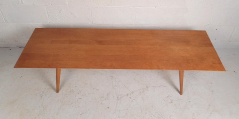 This stunning vintage modern maple coffee table features a rectangular top with splayed and tapered legs underneath. A stylish design by Paul McCobb that is sure to make a lasting impression in any modern interior. Please confirm item location (NY