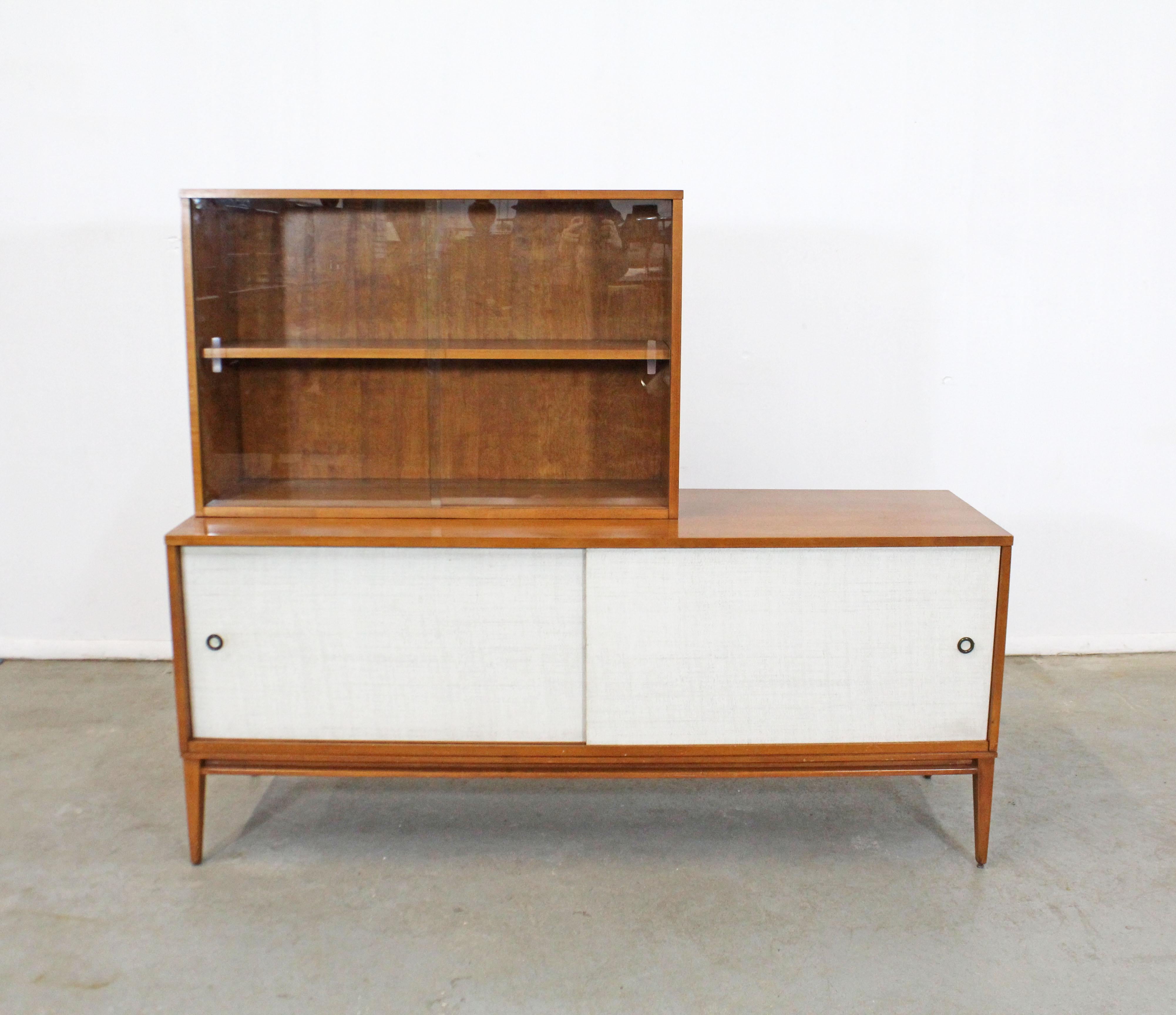 Offered is a vintage two-piece credenza designed by Paul McCobb for Planner Group. Features sliding glass doors and adjustable shelving on top, and sliding vinyl doors with shelving on bottom. It is in good condition considering its age, shows