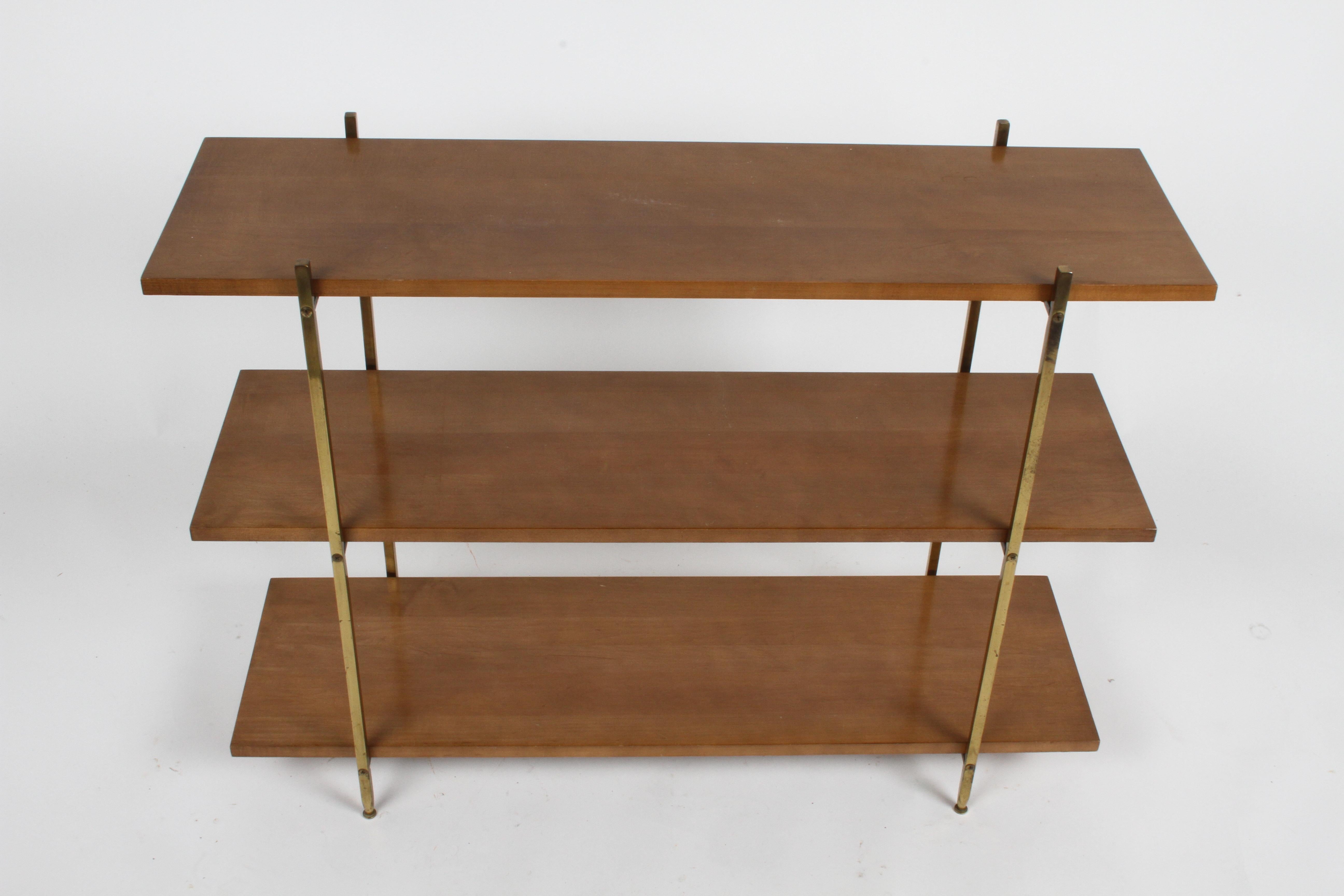 Attributed to Paul McCobb, this quality and heavy Mid-Century Modern three tier bookshelf or TV stand has the characteristics of a McCobb design, with the square brass and use of maple for shelves. The 1/2 square solid brass tapers at the end of the