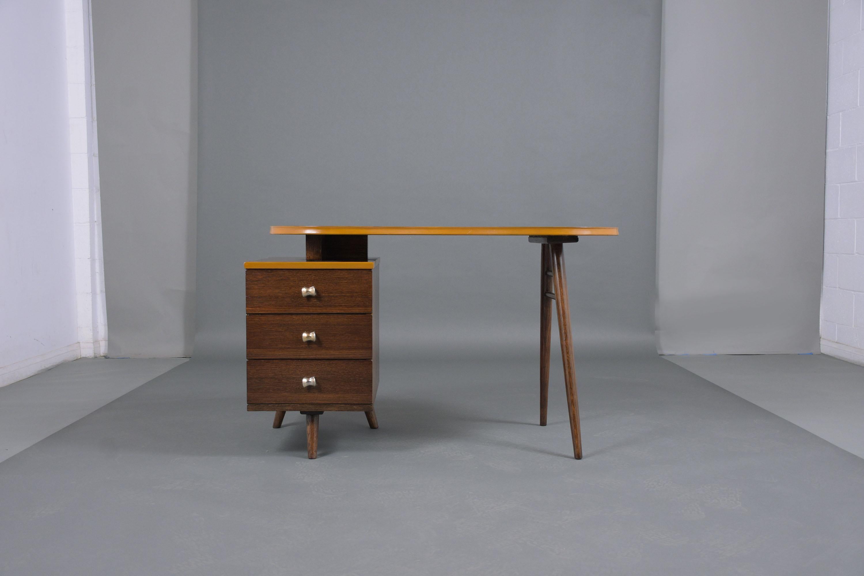 This mid-century modern pedestal desk is in good condition crafted out of oak wood and has been professionally restored by our team of expert craftsmen. This writing table has been refinished in walnut & raw sienna color moldings with a lacquered