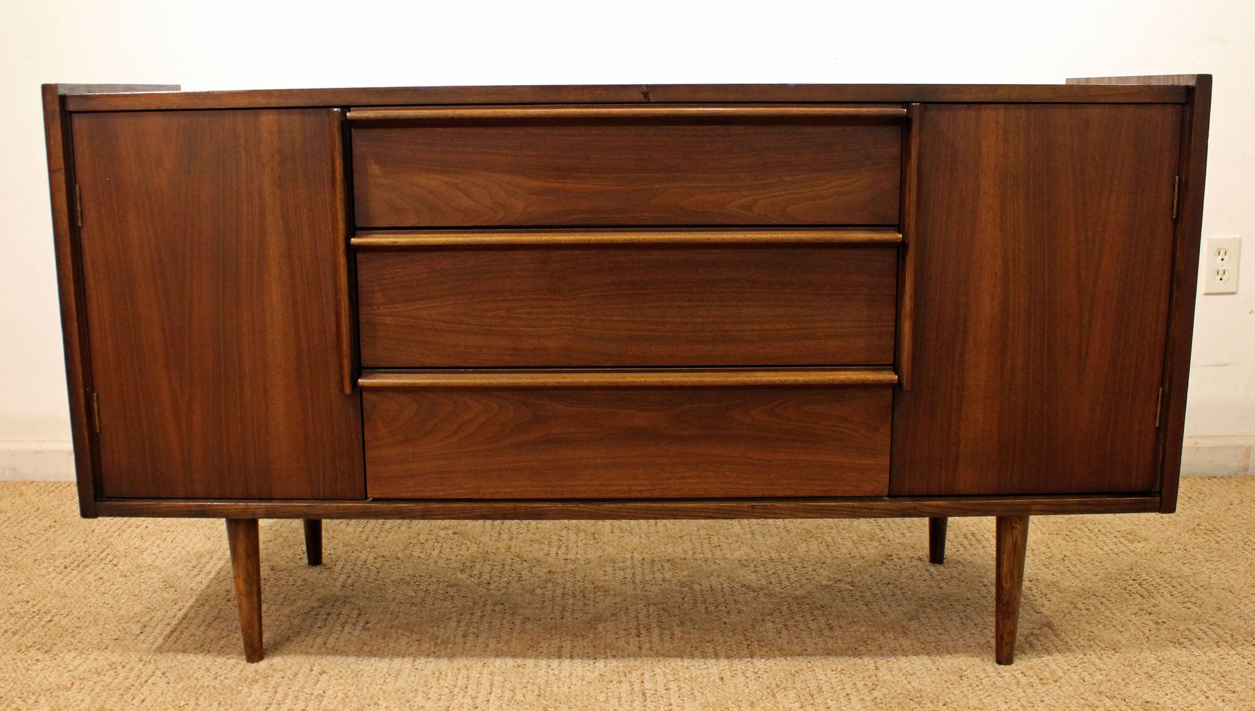 This credenza is made of walnut, has 2 doors on each side with shelving, and 3 middle drawers. Has been refinished.