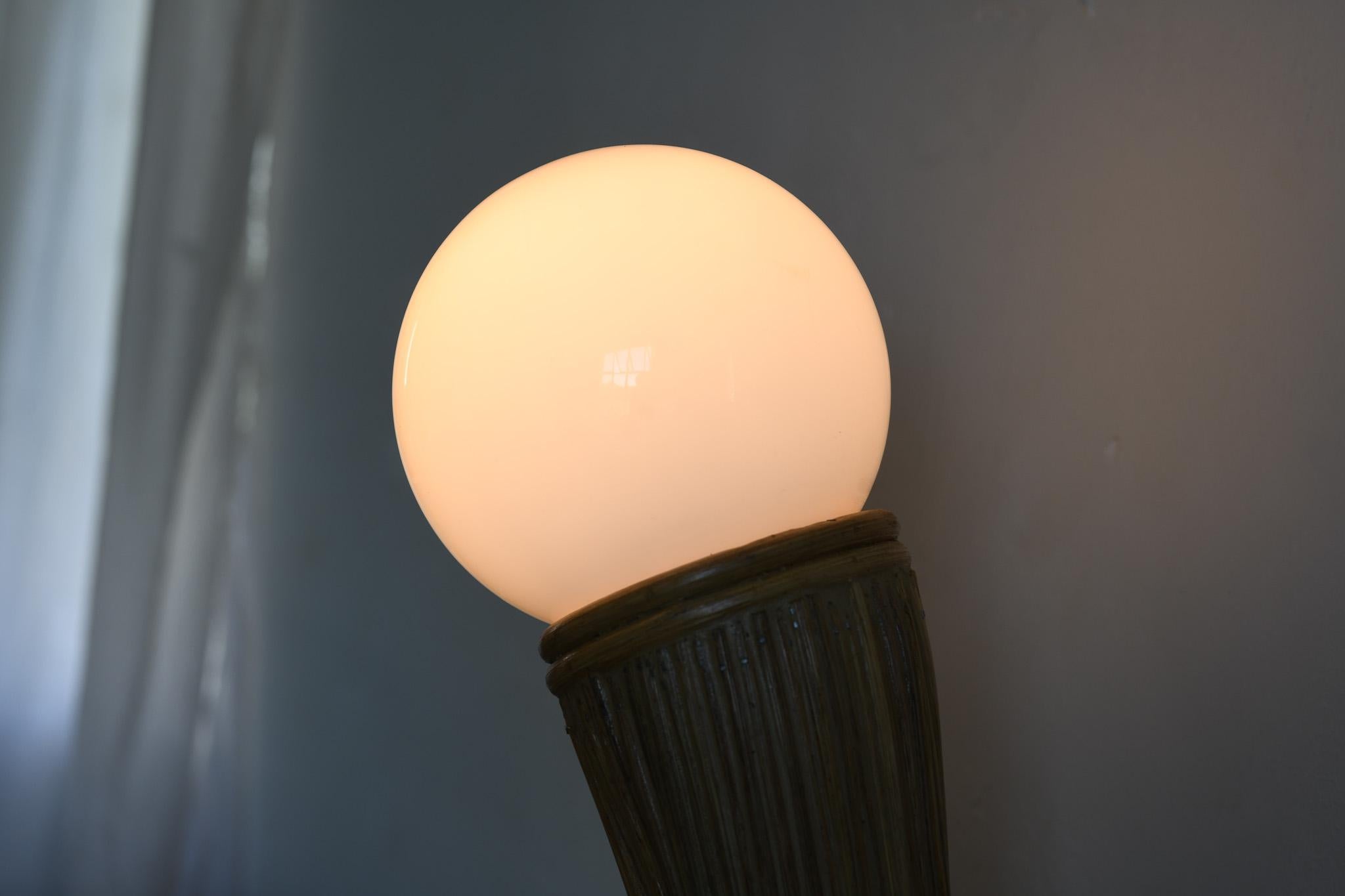 This lamp features a sleek mid century modern design with a base made of pencil reed and a space age inspired dome shade. It is both functional and stylish, perfect for adding a touch of retro cool to any space. The unique combination of materials