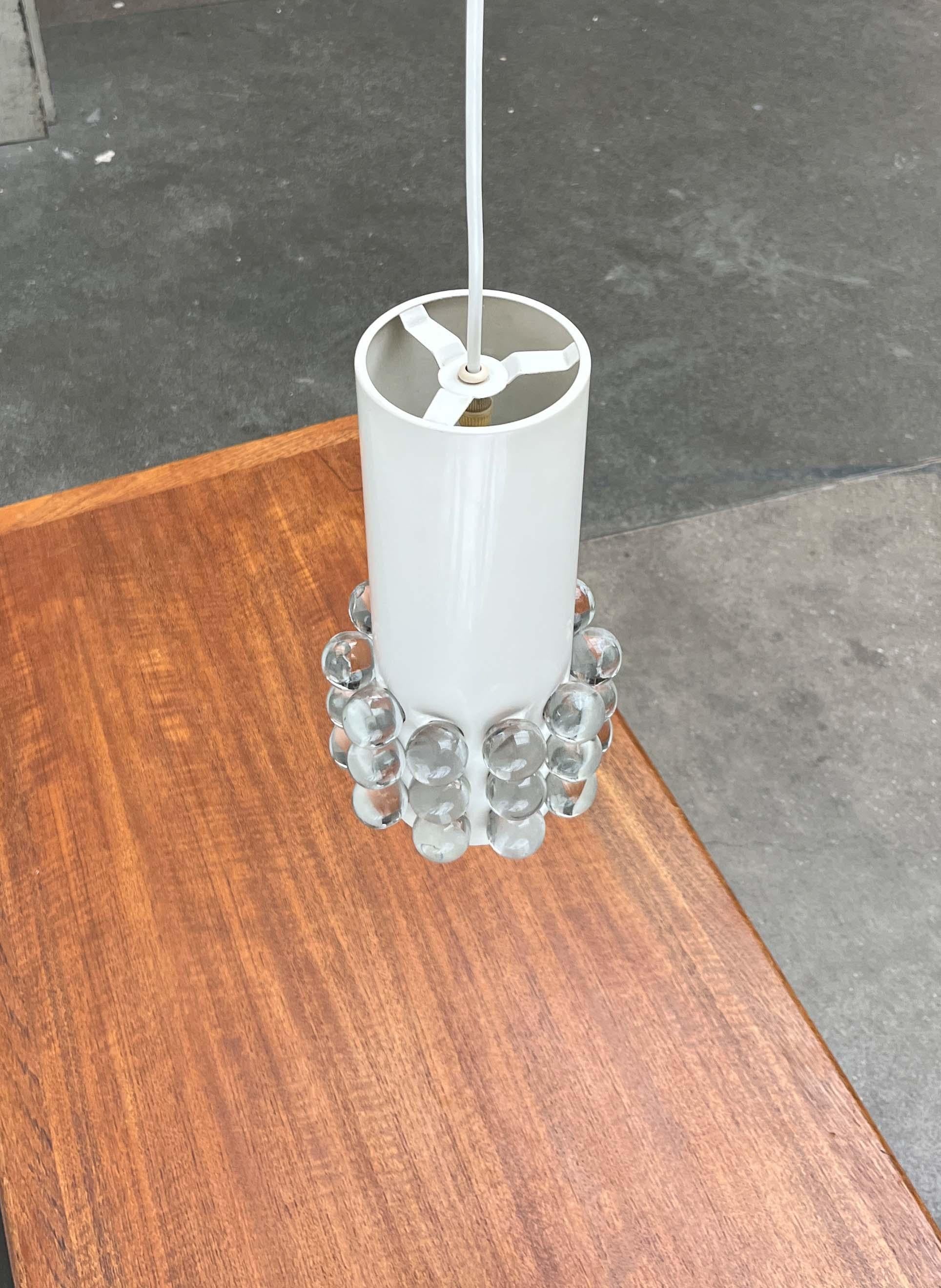 Impressionnante lampe suspendue avec des boules en acrylique.
 
Le corps de la lampe est constitué d'un simple cylindre métallique peint en blanc. Le tiers inférieur présente des perforations symétriques. Les grands trous sont fermés par des boules