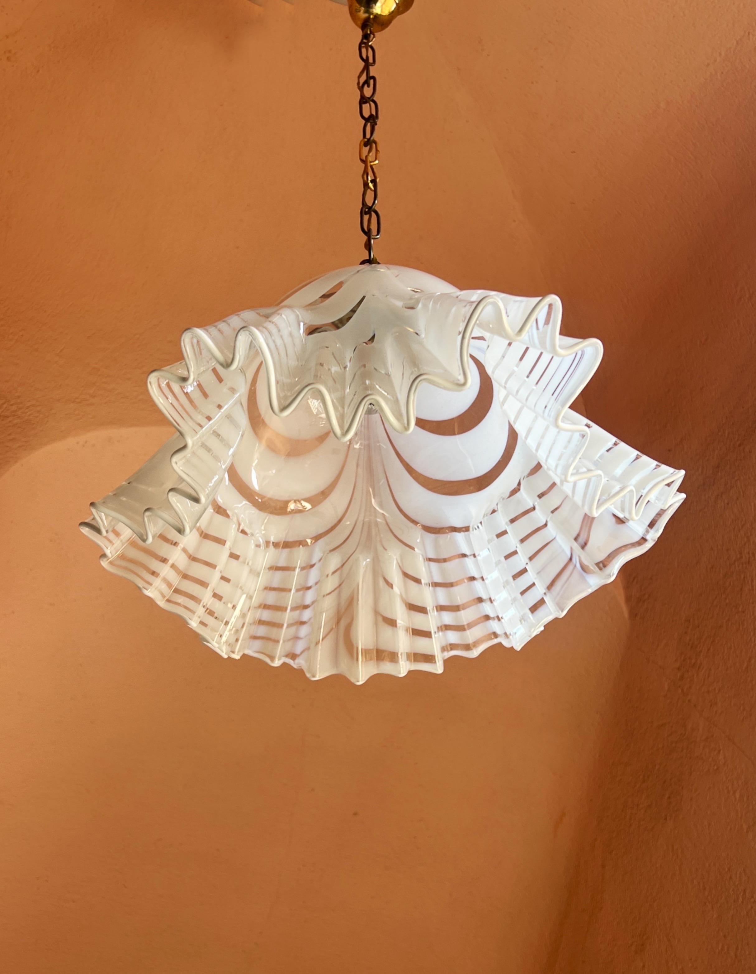 Esta lámpara colgante de la Era Espacial, fabricada en cristal de Murano soplado a mano con franjas blancas y transparentes, se atribuye a Venini y data de alrededor de 1970. La luz tiene una cadena metálica. La altura con la cadena es de 80 cm
