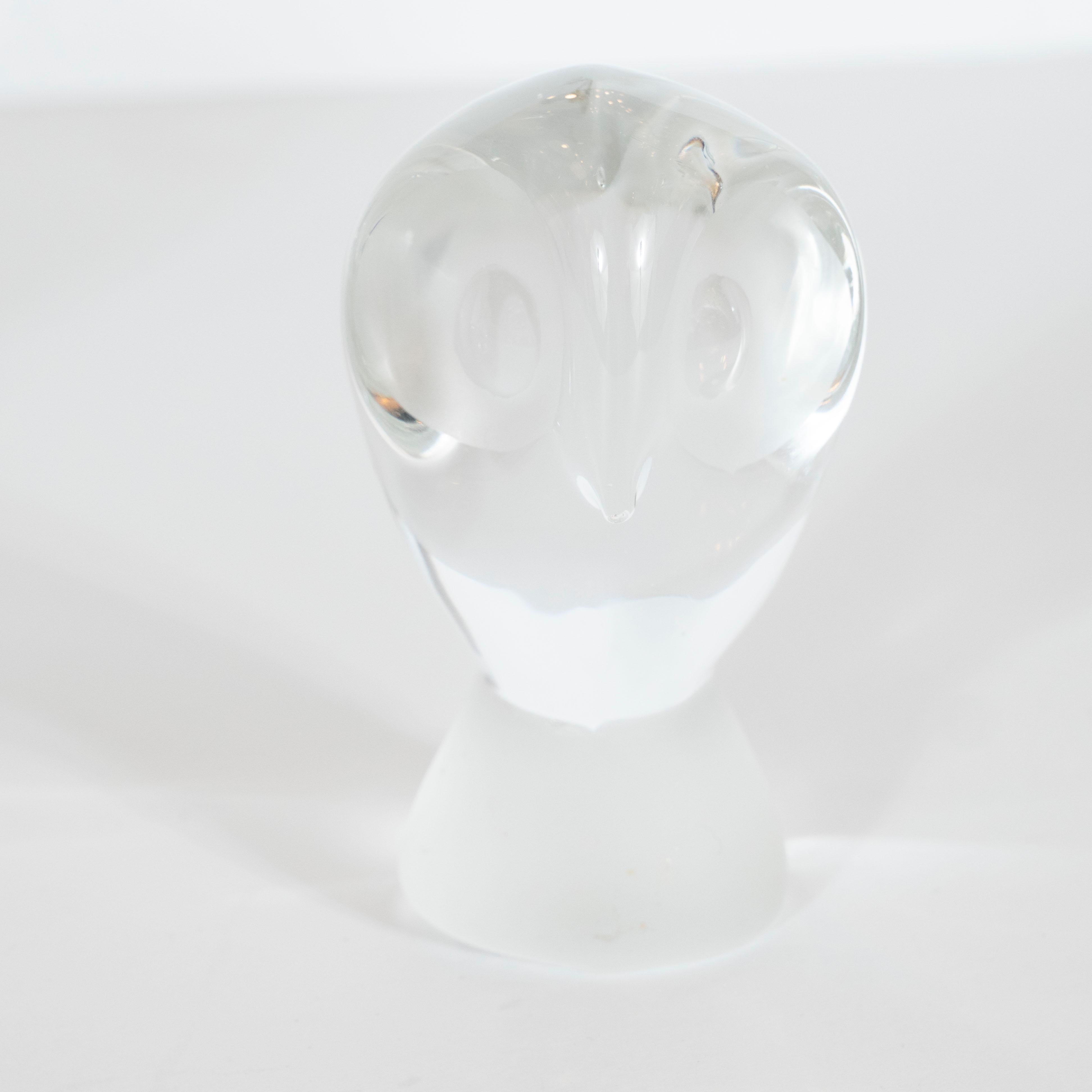 This glass paperweight/ decorative object was handmade in the United States circa 1960. It offers an abstracted rendition of a perched owl. The Owl's face is divided in half by a gestural beak, its eyes are fire polished hemispheres set in
