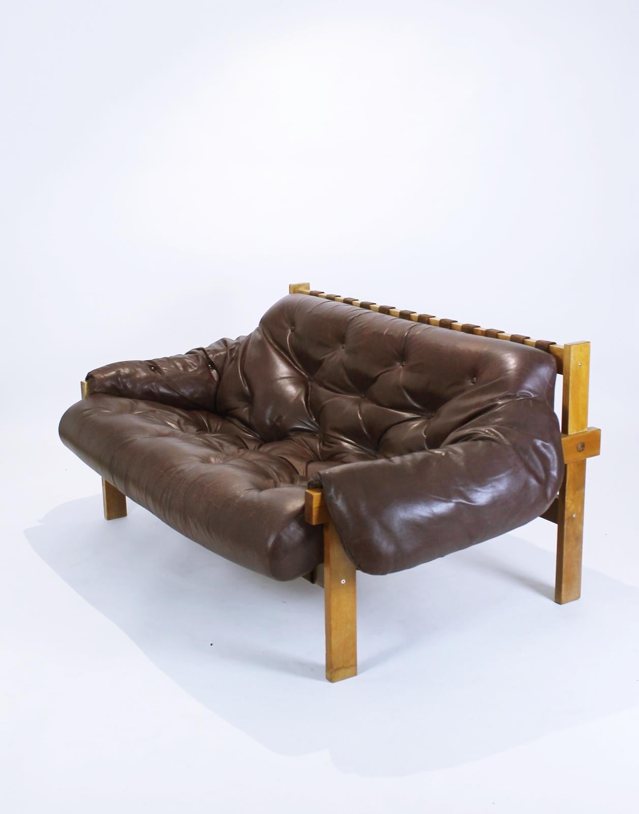 Wonderfully distressed brown leather sofa in manner of Brazilian designer Percival Lafer. Featuring a solid wood frame with beautiful grain that supports the natural leather straps which the tufted brown leather cushion rests on. The original