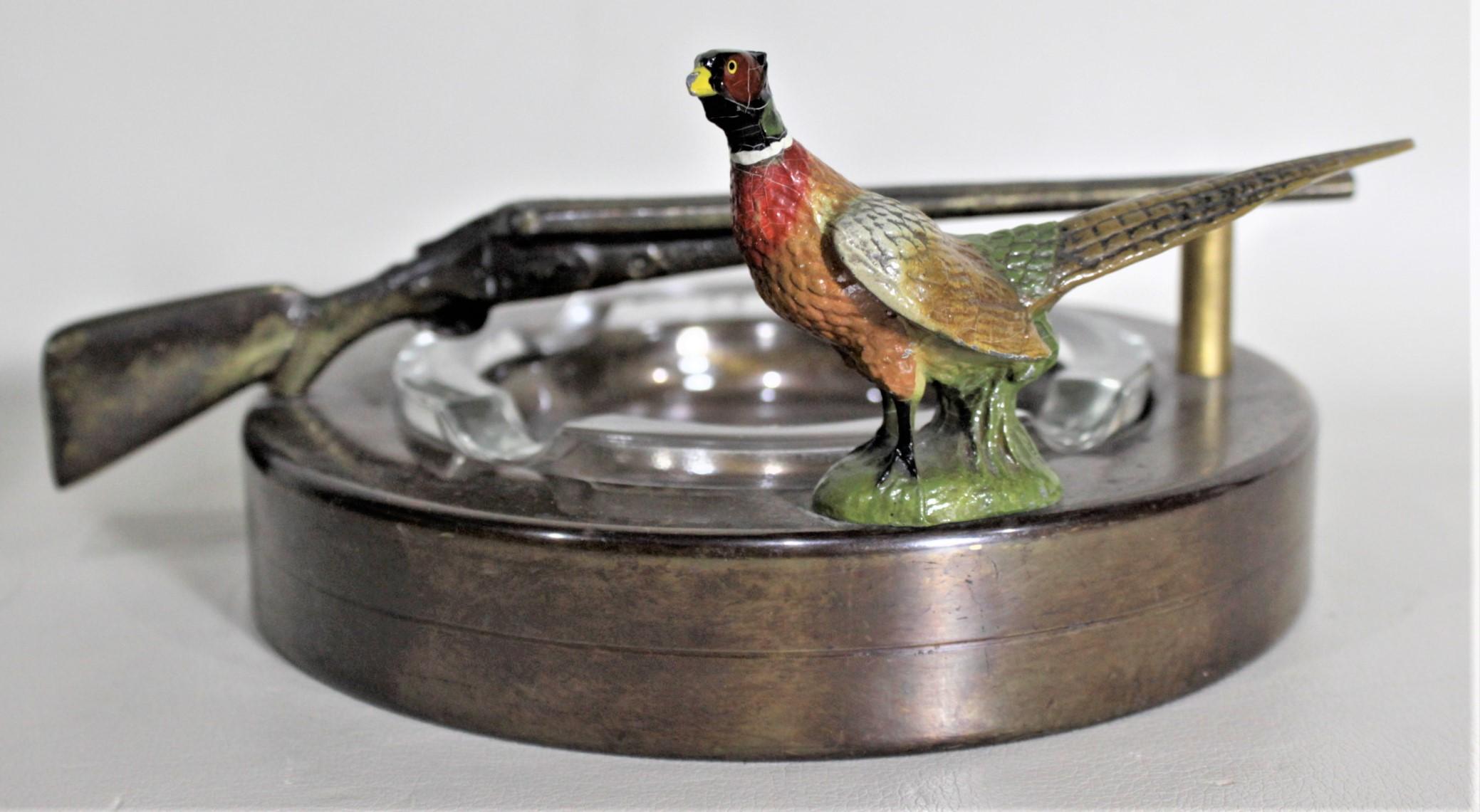 This Mid-Century Modern ashtray is unsigned but presumed to have been made in the United States in circa 1965. This ashtray features a cast and cold-painted figural male pheasant on one outer edge and a figural double-barreled shotgun as a handle.