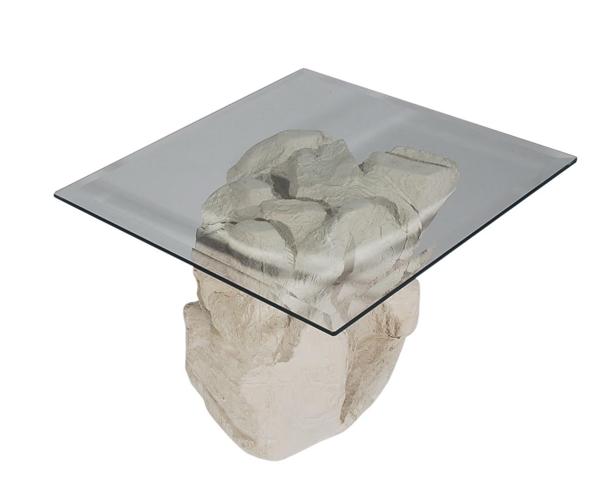 A sculptural faux rock formation table made by Sirmos in the 1970s. It features a plaster molded rock formation base with a clear glass top.
   