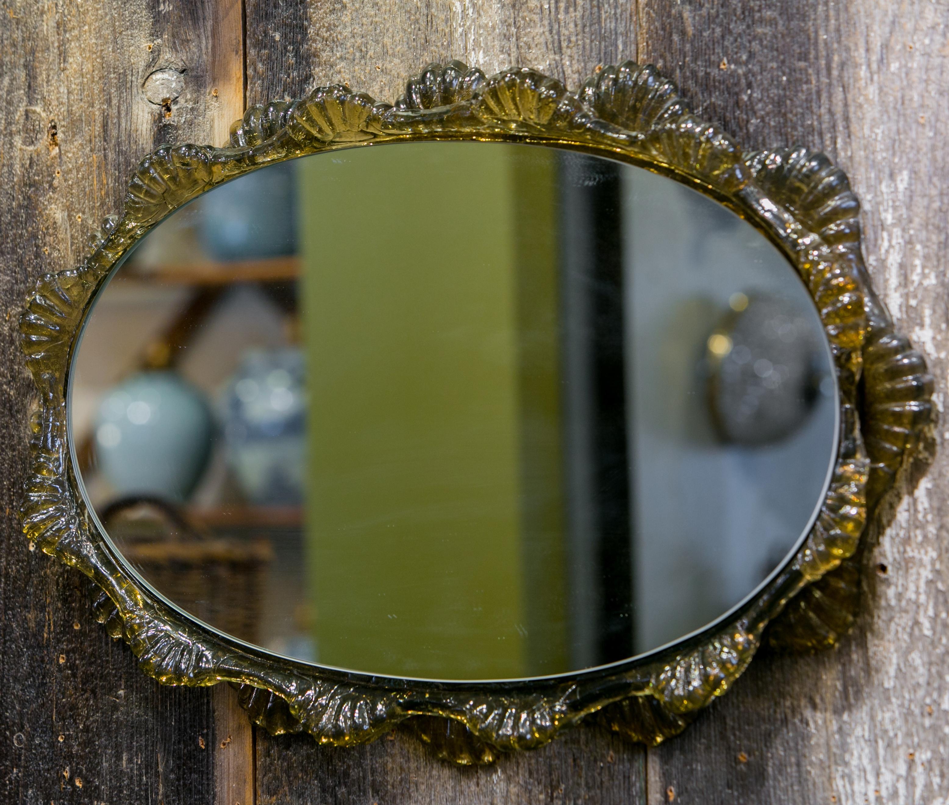 Mid-century polycarbonate mirror that mimics Murano glass. This interesting mirror appears to be glass, but is plastic. Its color is kind of a semi-transparent green tea color. All original and a nice accent to any room.