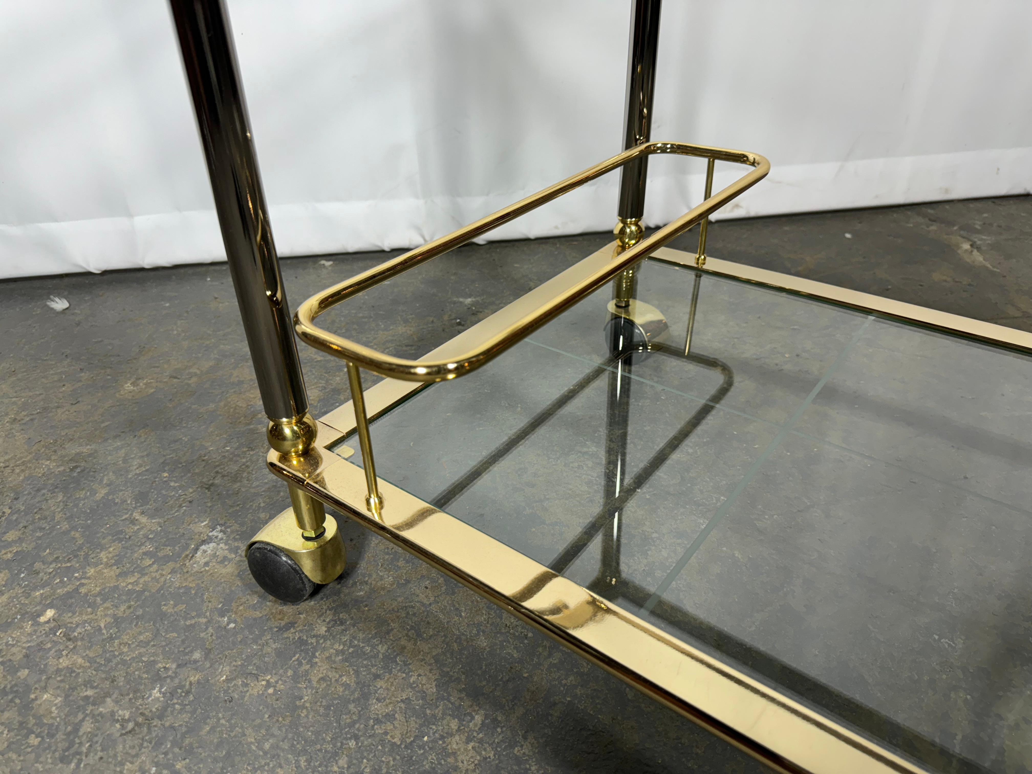Chariot de service à deux niveaux sur roulettes en laiton poli, datant du milieu du siècle dernier, vers 1960. Construite en laiton et de forme rectangulaire, la desserte à deux étages est un véritable trésor pour l'art culinaire.  ou le chariot de