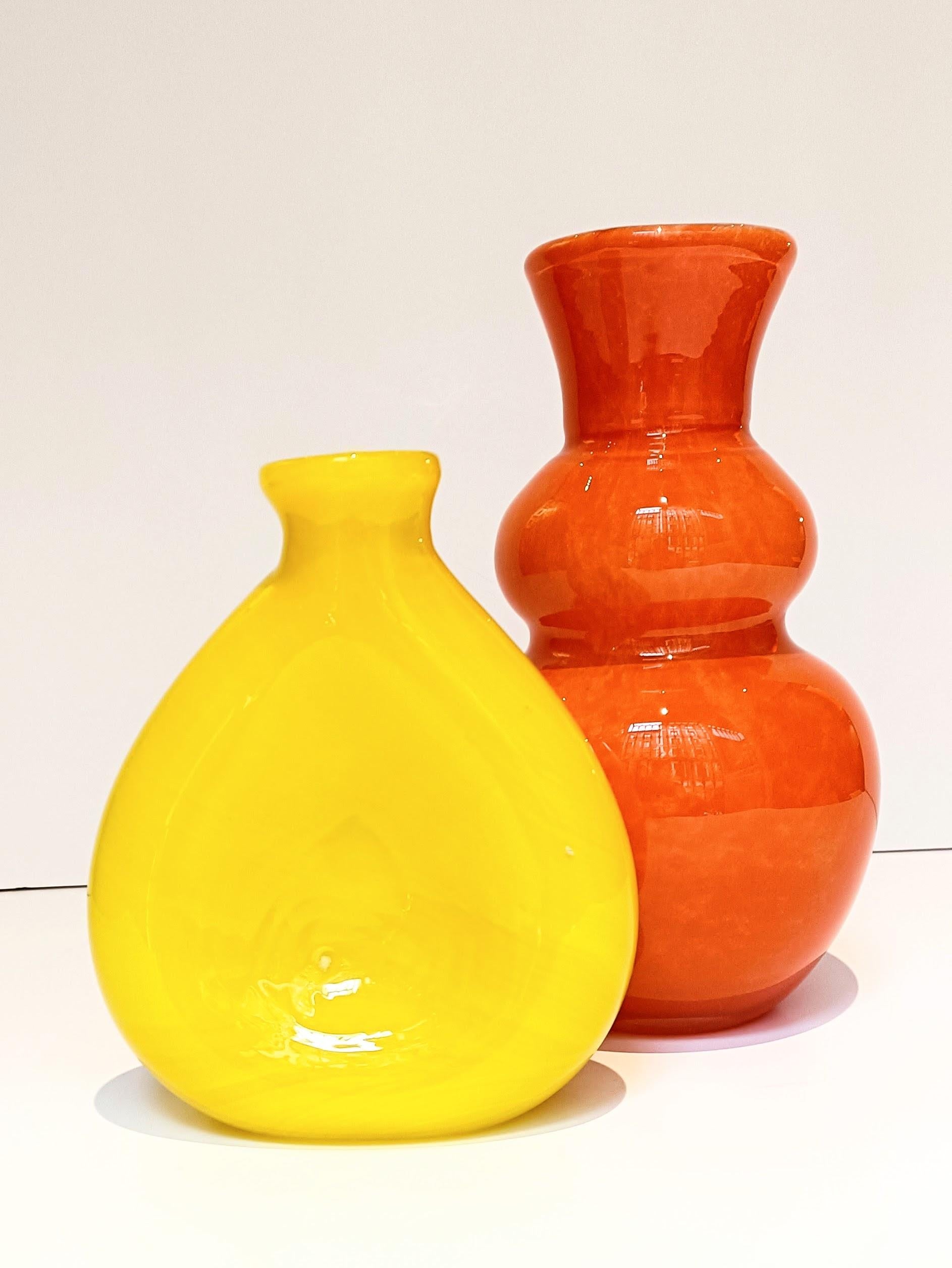 Pair of vintage Pop Art style Mid-Century Modern Murano glass vases. Their thick exterior layers in vibrant orange and yellow hues, along with the distinctive white casing on the orange vase, add a striking visual appeal. They were handcrafted in