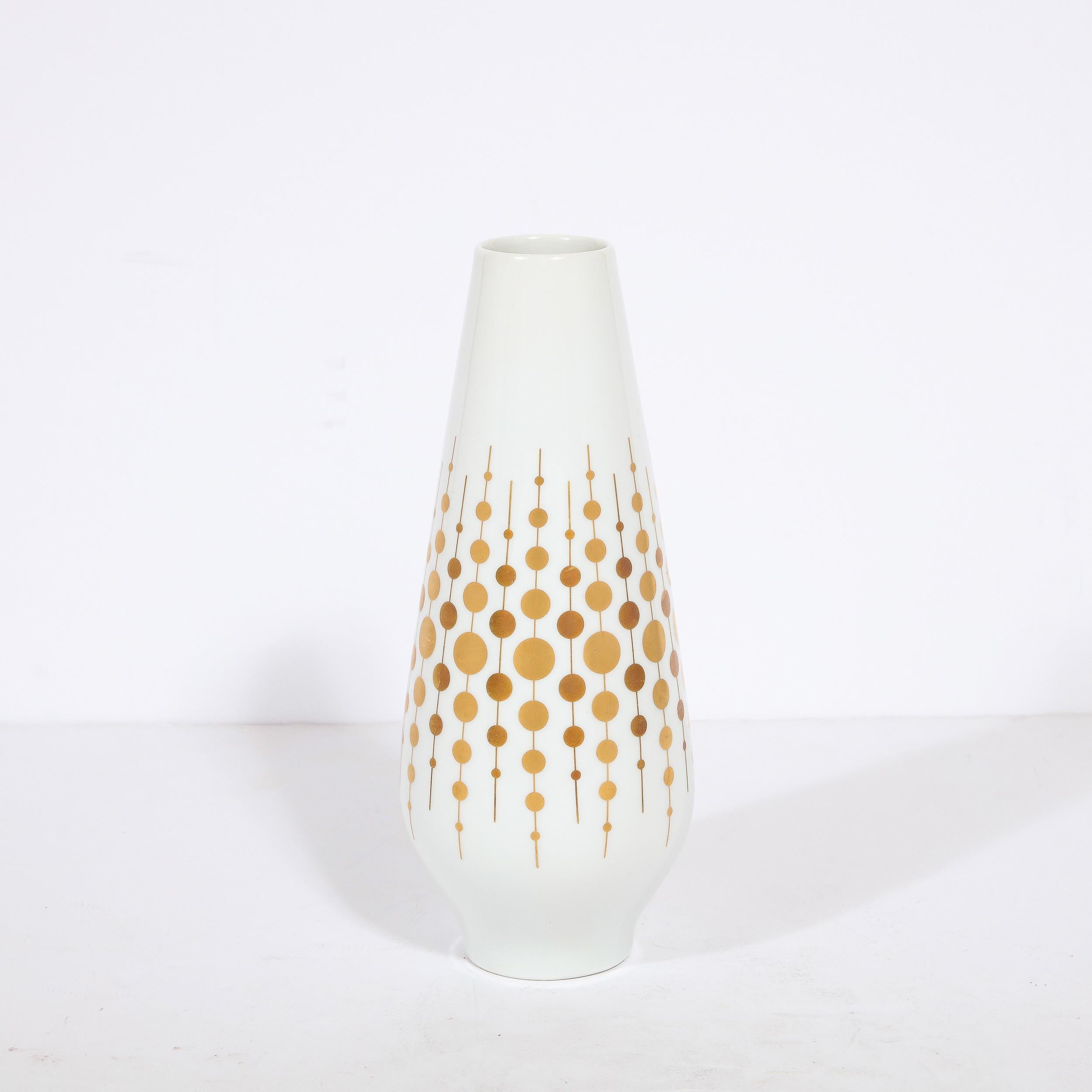 This refined Mid Century Modern porcelain vase was realized by the esteemed maker Alka Kunst in Germany circa 1960. It features a cylindrical body in white porcelain that flares subtly from its circular base then tapering to a round mouth. The