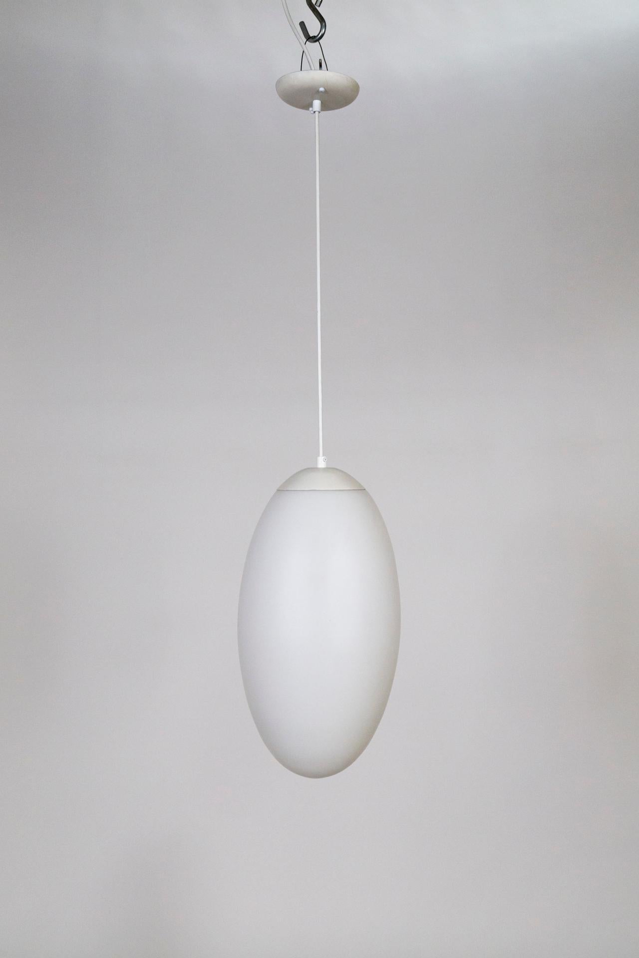 Long, oval shaped, milk glass pendant; seamlessly capped with white steal and cord. Made by Prescolite; rare and in great condition. Original canopy with maker's mark. Can be hung indoors or out. Measures: 20