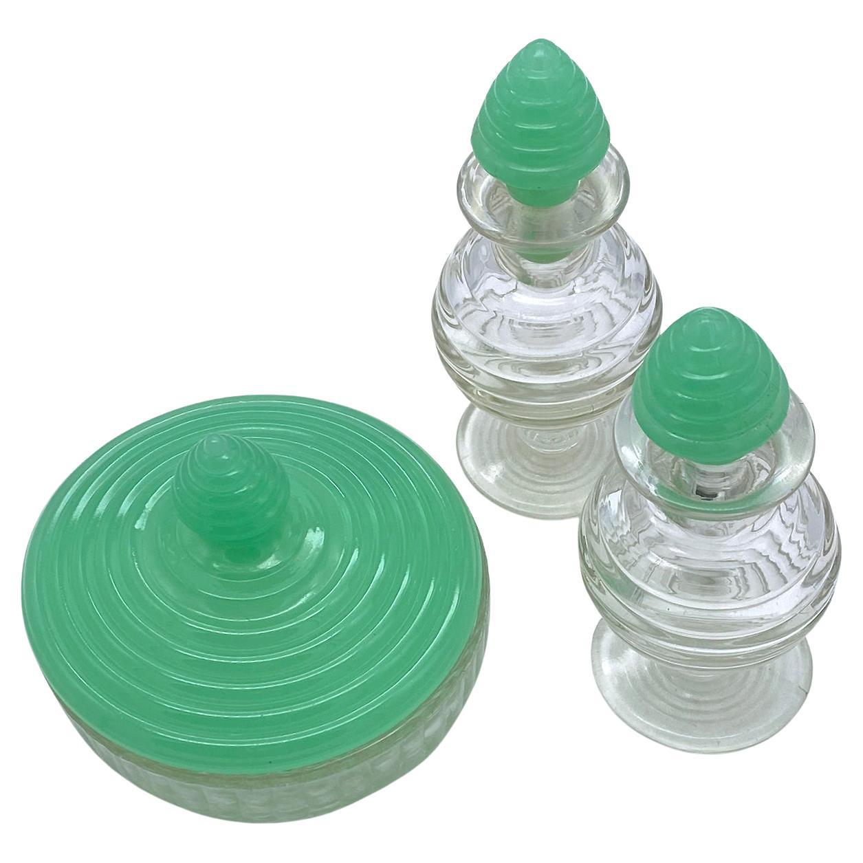 This is a Mid Century Modern pressed glass vanity set. The set includes two perfume bottles and one powder box. These three clear optical pressed glass dresser decorative pieces come with Kelly Green stopper/lids. The perfect touch for your vintage