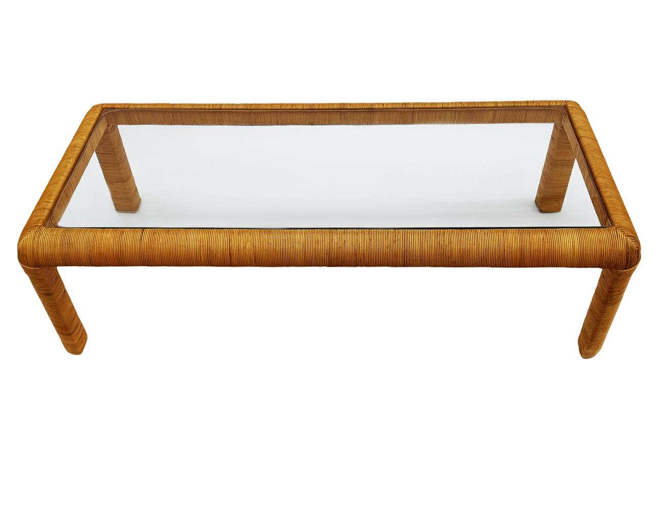 A long rectangular coffee table circa 1970's in the style of Paul Frankl. It features a curved rattan frame with a clear glass inlayed top. Clean ready to use condition.
