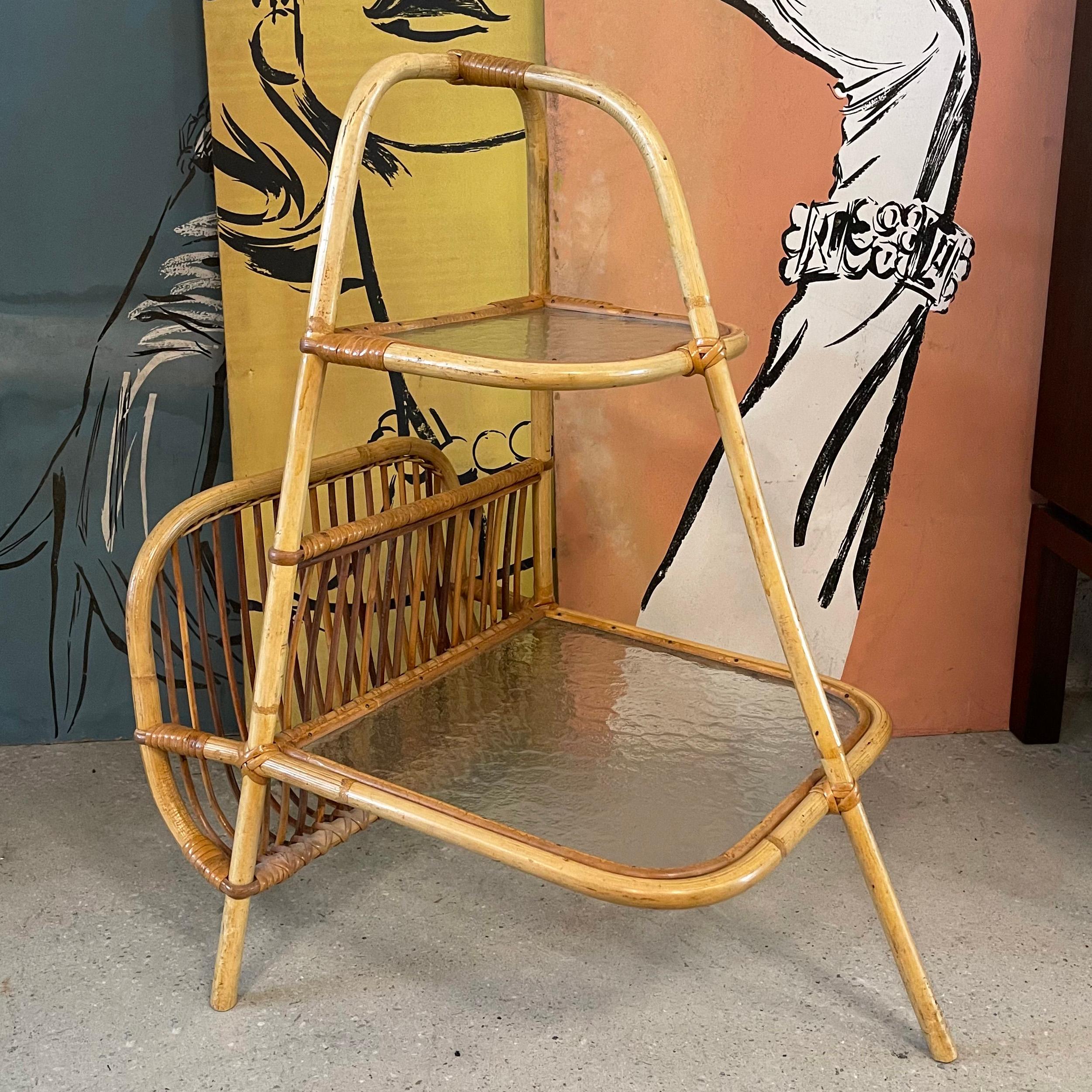 Mid-Century Modern, tiered side table with magazine holder features a rattan frame with textured glass shelves. The tiers are 7 inches ht and 20 inches height.