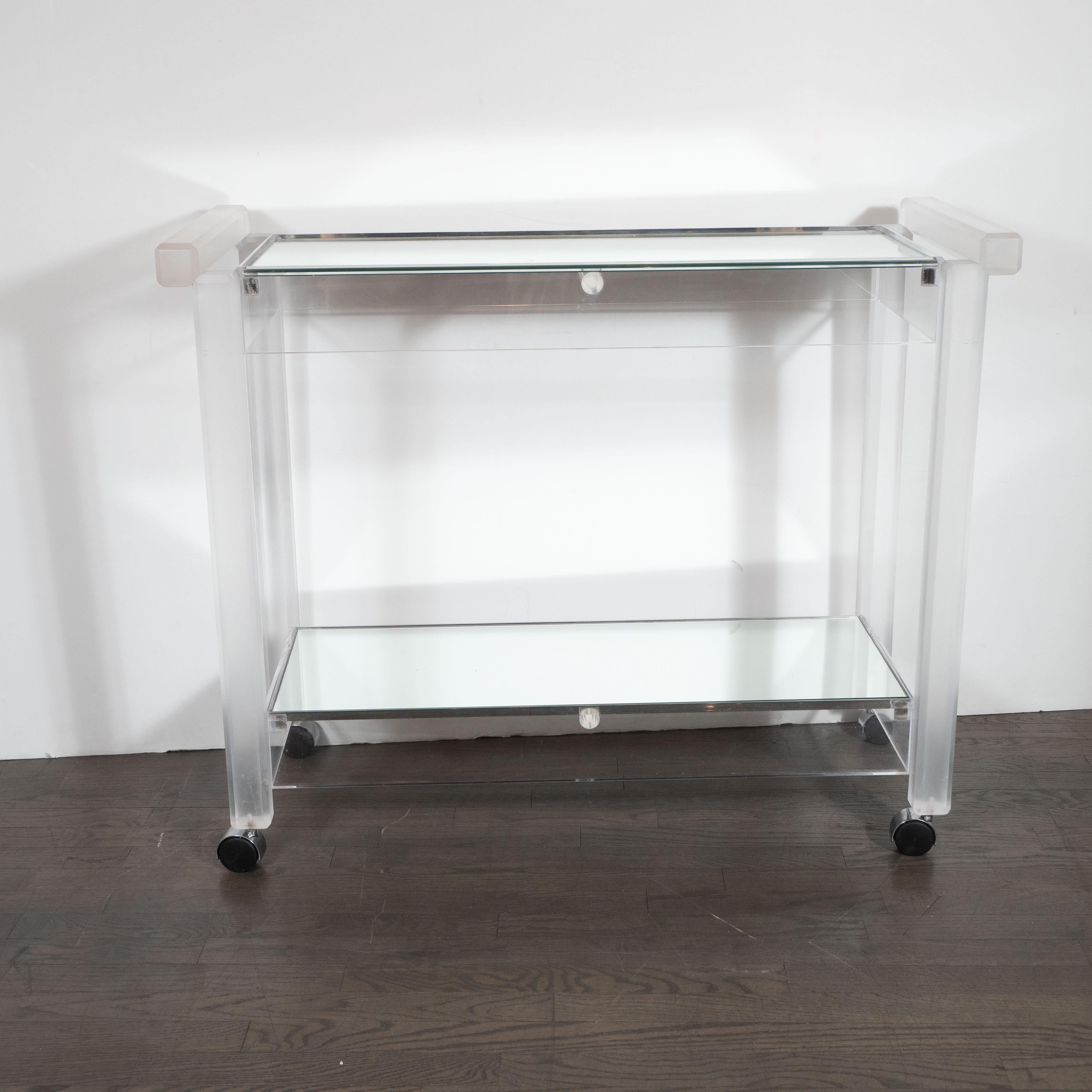 This refined and sexy bar cart was realized in the United States circa 1970 by the esteemed maker The Lion Frost Company. It features a rectilinear body composed of frosted lucite with two mirrored trays- perfect for storing bottles and bar