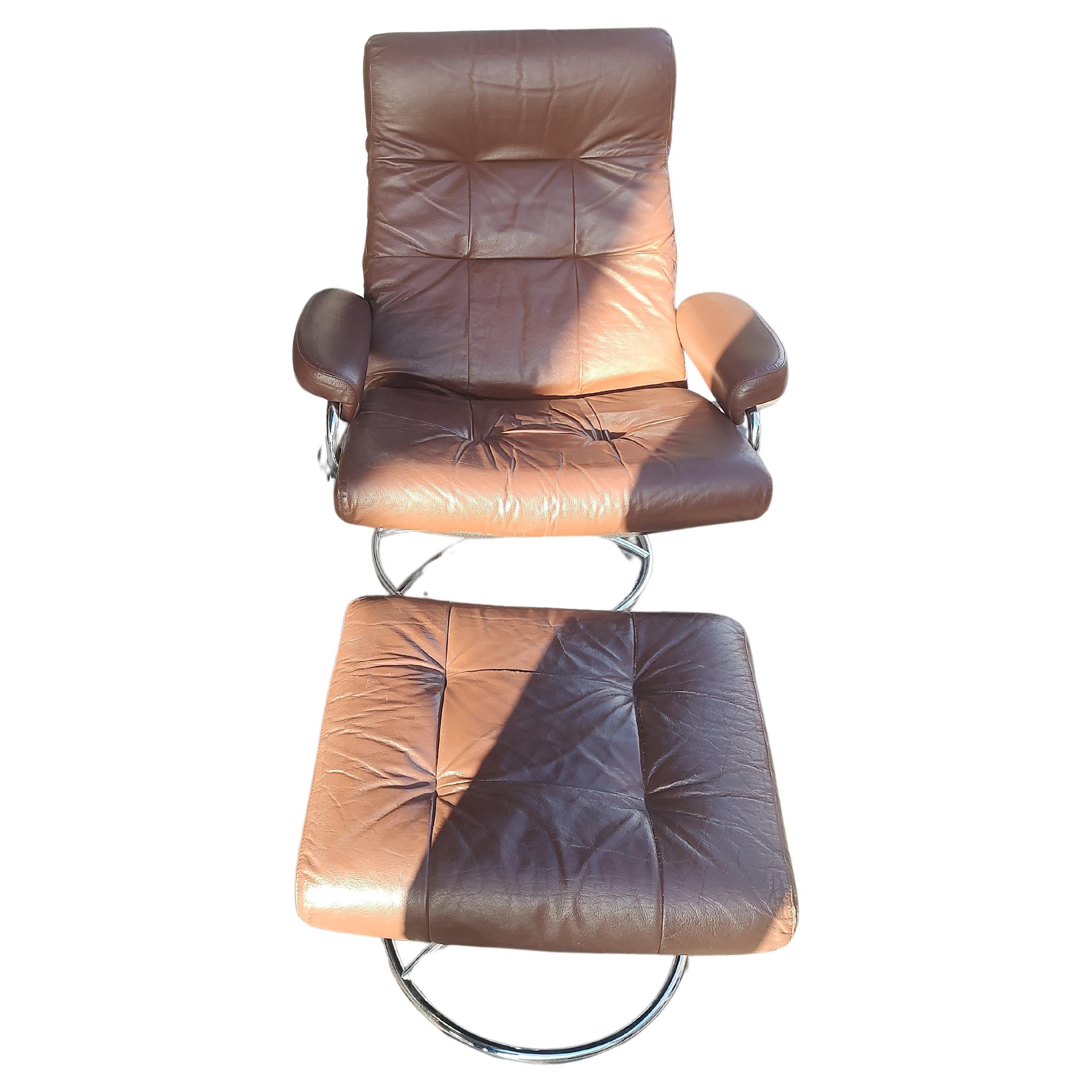 Fabuleux fauteuil inclinable Stressless Lounge de 1970 avec ottoman, fabriqué par Ekornes en Norvège. Le cuir marron est en excellent état avec un petit pli sur l'ottoman. Le chrome est vif et brillant. La mécanique est excellente. Le pouf est 22 x