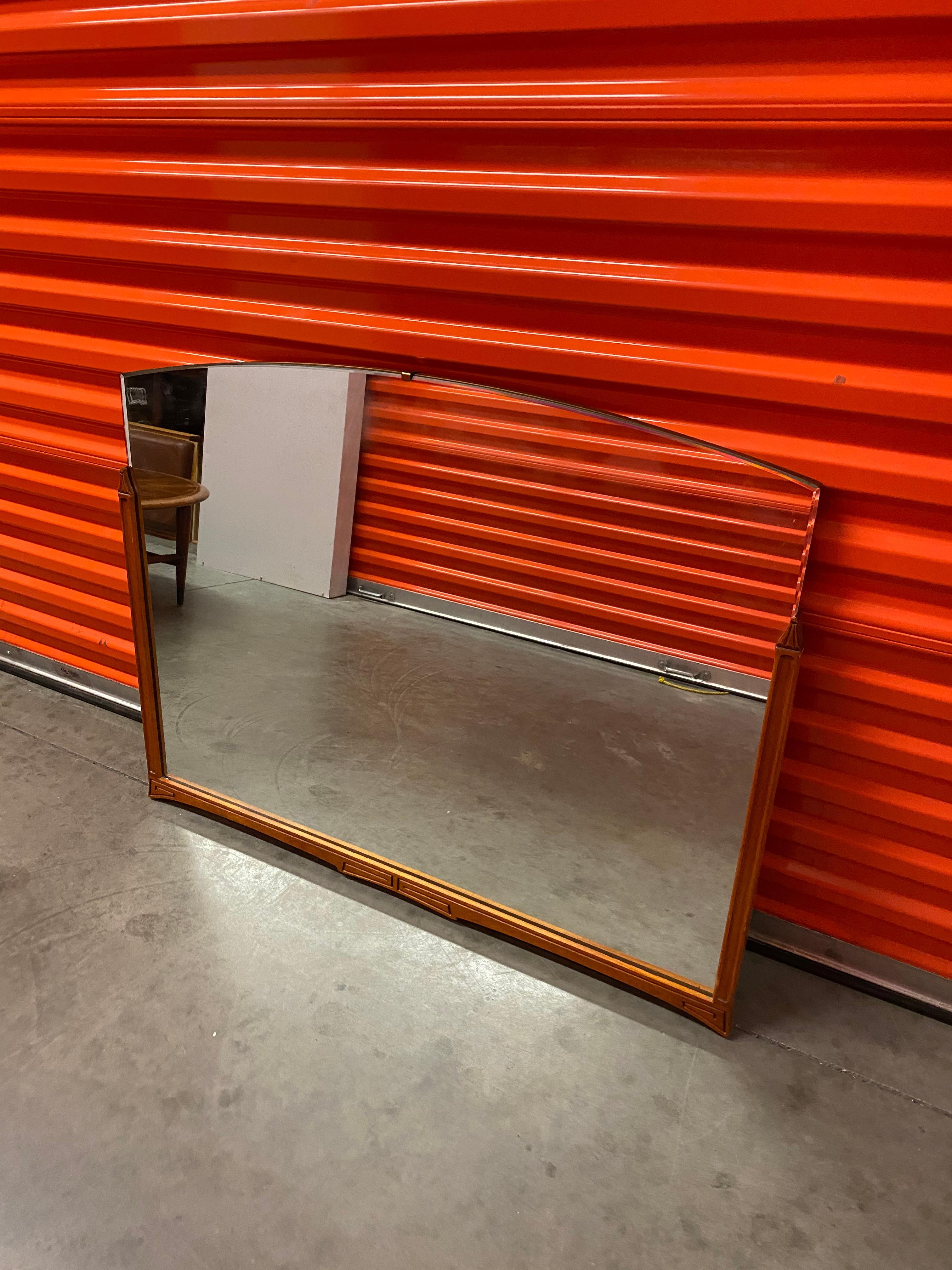 Mid-Century Modern rectangular wood wall mirror. Hanging wall mirror with exposed beveled edge at top and wood frame at lower portion. Simple decorative details at wood edges and frame give this piece its character.