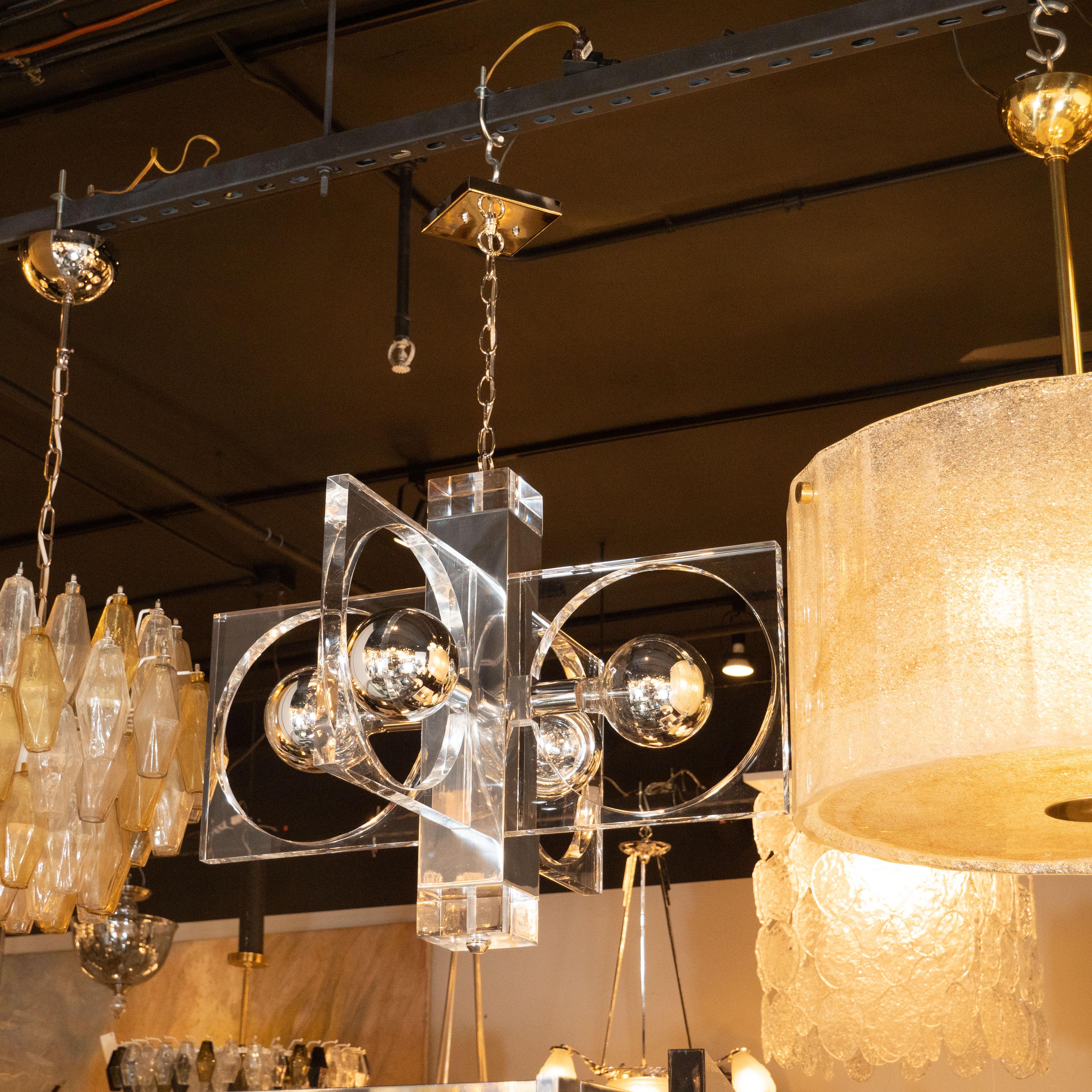This chic and graphic Mid-Century Modern chandelier was realized in the United States, circa 1970. It features a volumetric rectangular chrome body with Lucite caps on each end. Four square Lucite forms emanate outwards from each face of the body