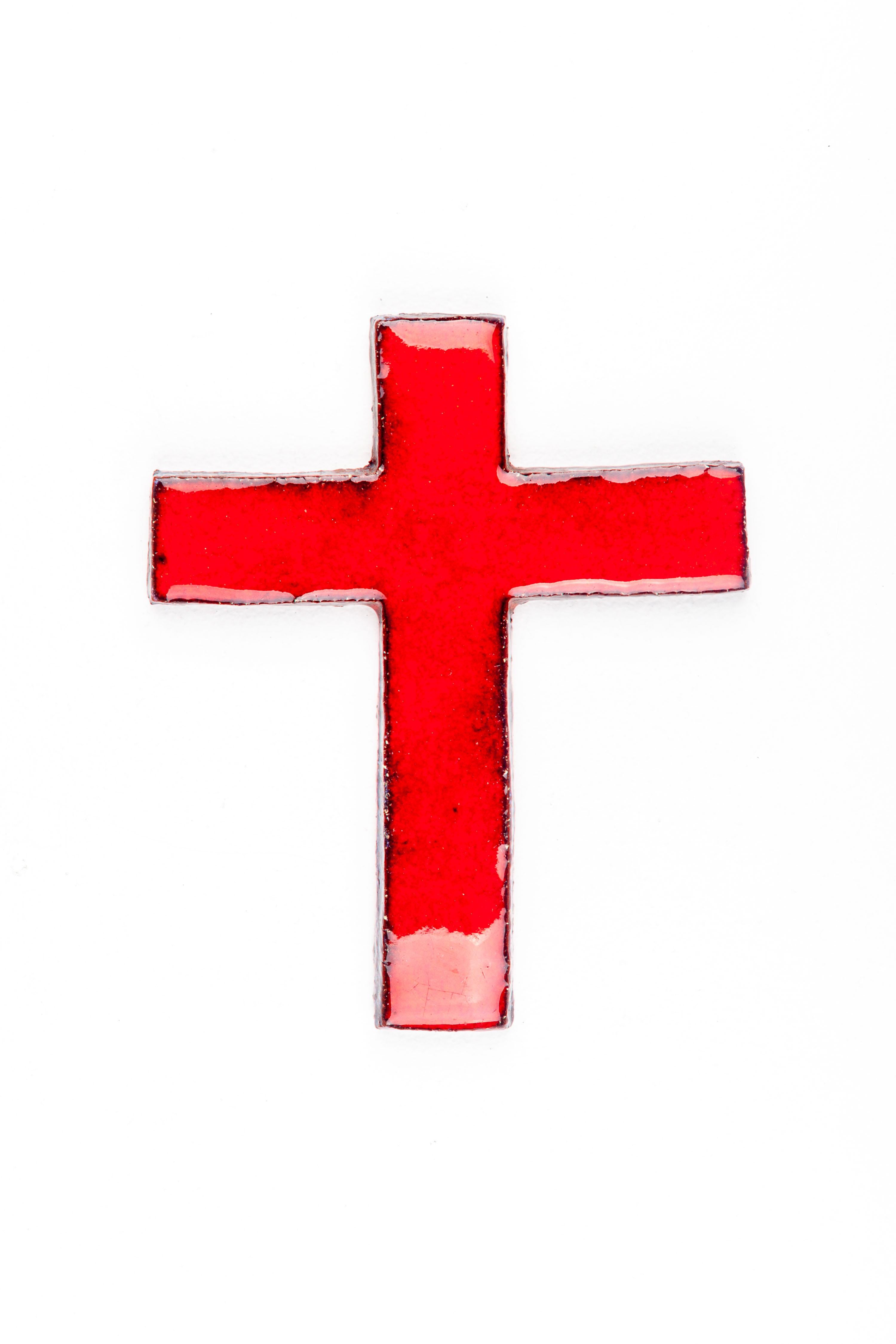 This handcrafted ceramic cross is a distinctive artifact of mid-century modern design, created by European studio pottery artists renowned for their innovative approaches to traditional forms. The cross, with its bold red glaze, stands out as a