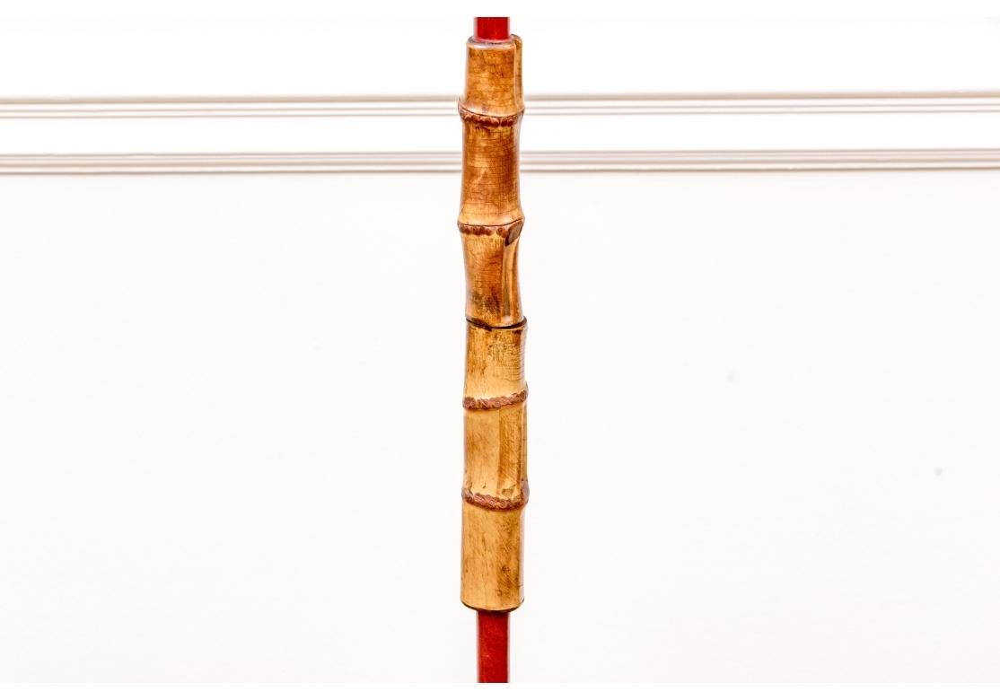Una fantastica lampada da terra in ferro della metà del secolo scorso, avvolta in pelle rossa e decorata con meravigliose sezioni di bambù marrone chiaro e miele alla vita e alla base su un treppiede di piedini. Sormontato da un paralume bianco su