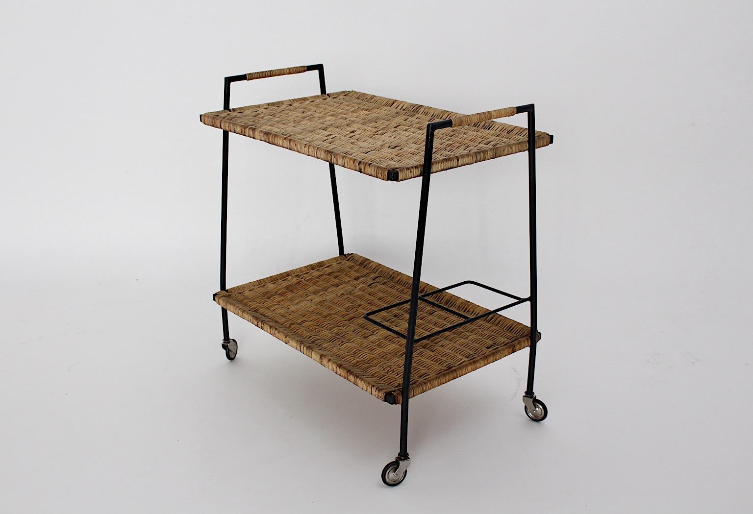 Mid-Century Modern Riviera style vintage bar cart or serving table from rattan and black lacquered metal with two trays and four wheels designed 1950s Austria.
Amazing bar cart with woven rattan network trays and partly wrapped handles in good and
