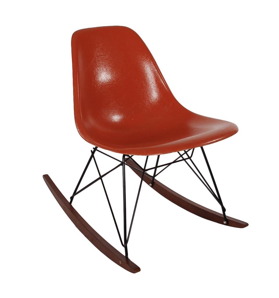 A beautiful retro orange fiberglass rocking chair designed by Charles Eames for Herman Miller. It features a vintage fiberglass shell chair on a newer production rocker base. Embossed manufacture logo on bottom of chair.