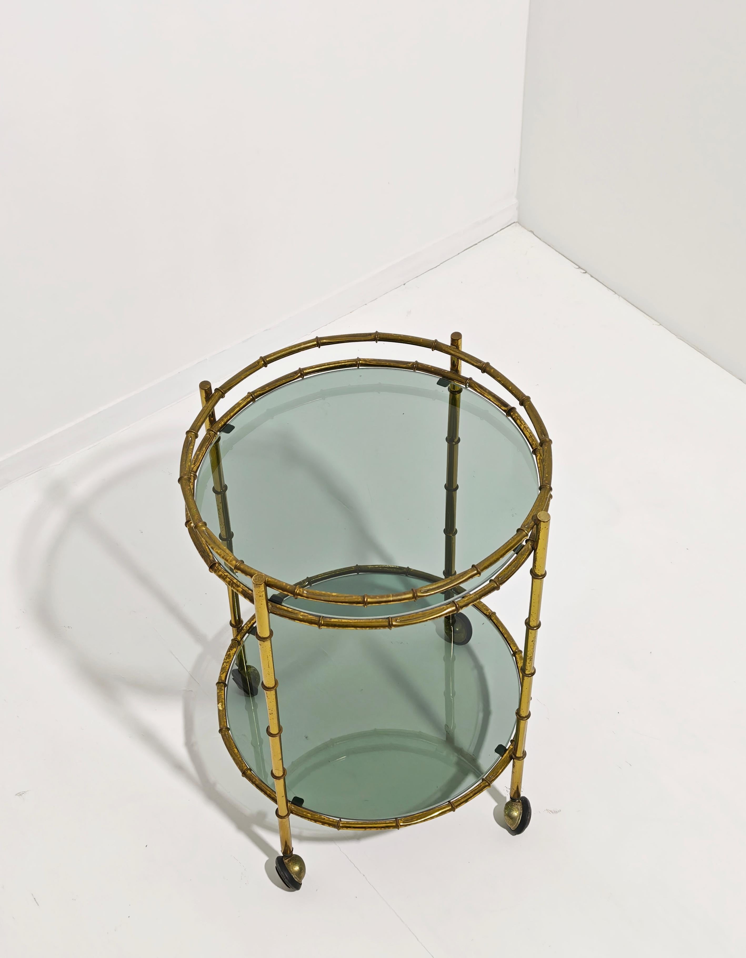 Chariot de cuisine en laiton effet bambou avec étagères en verre fumé. Fabriqués en Italie dans les années 1960 et 1970. Quatre pieds soutiennent les plateaux de verre supérieur et inférieur. De forme circulaire, il est doté de quatre roulettes