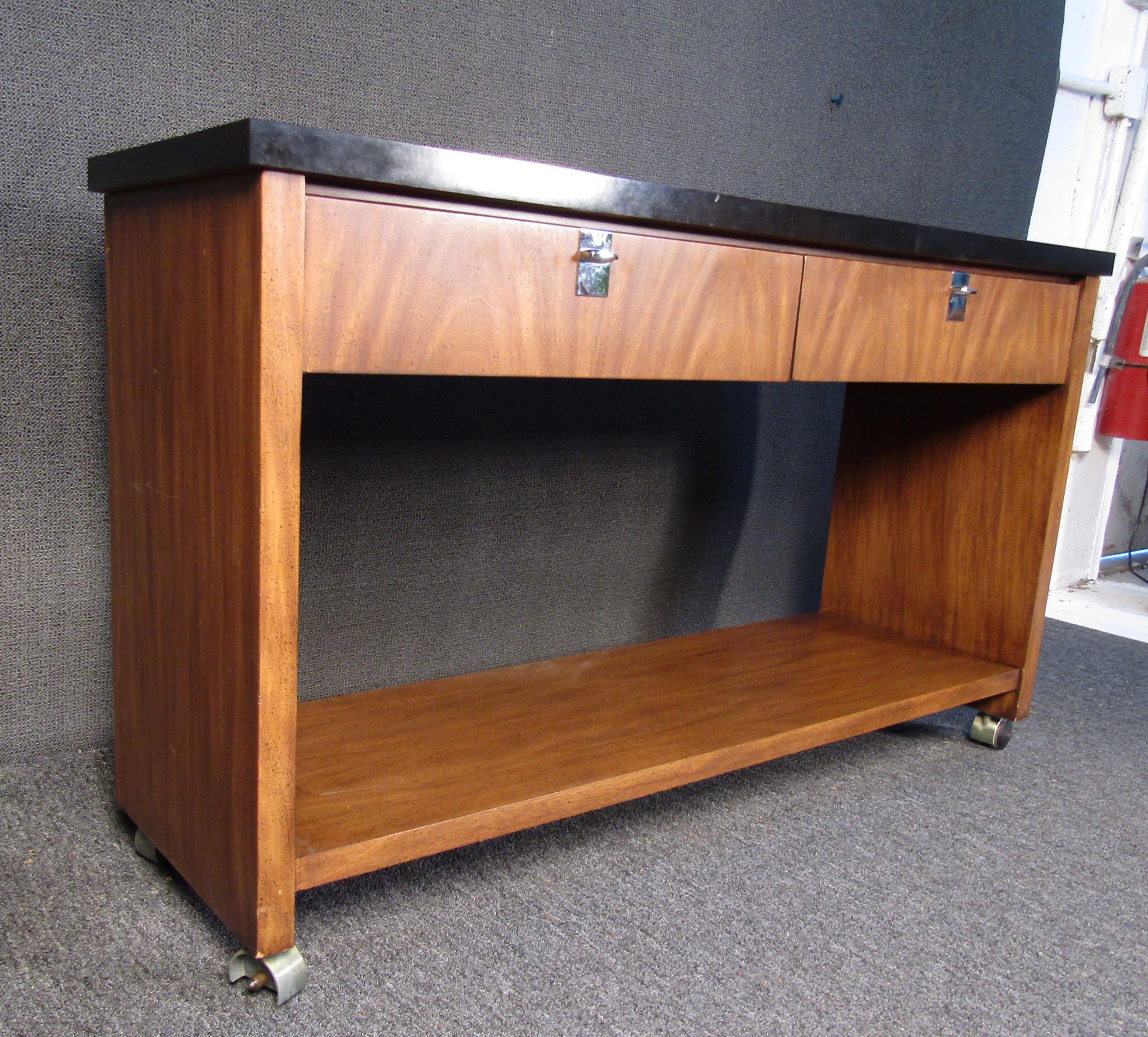 An incredible console table by J.B. Van Sciver, this Mid-Century Modern style table would be a stylish addition to any home or office. Two large drawers offer ample storage, while a black top surface compliments rich walnut woodgrain.