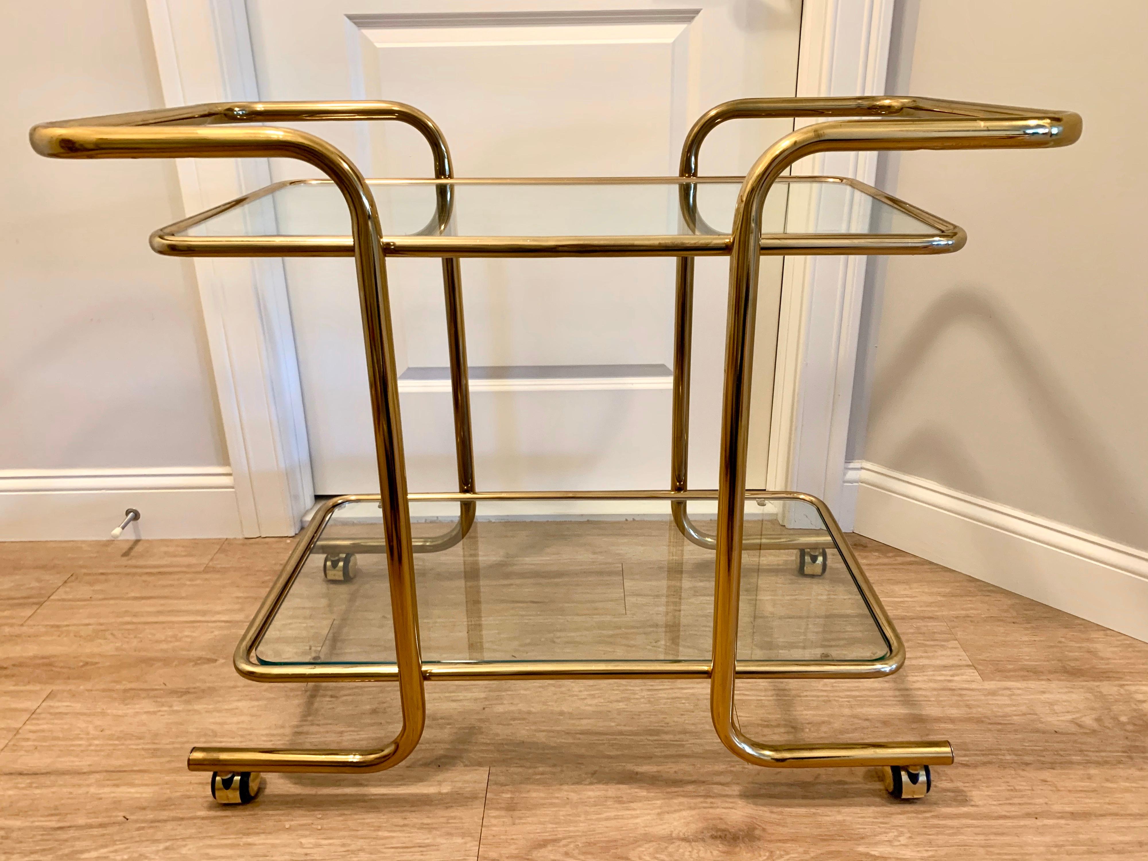 Midcentury heavy brass tubular and glass two tiered rolling bar cart. Brass castors. Can be pushed or pulled on both ends.