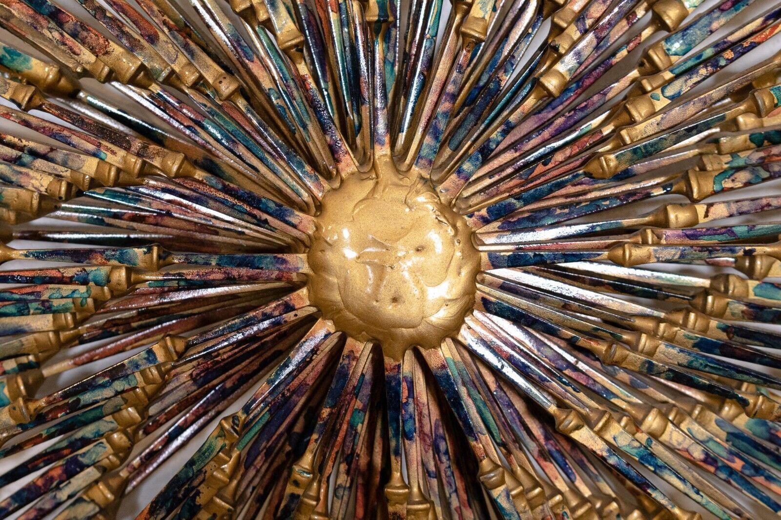 A marvelous brutalist wall sculpture made of metal and iron nails by Ron Schmidt. In a starburst/sunburst/pinwheel design that is highly sought after for a Mid-Century Modern aesthetic. This sculpture has a unique finish of metal coating with gold,