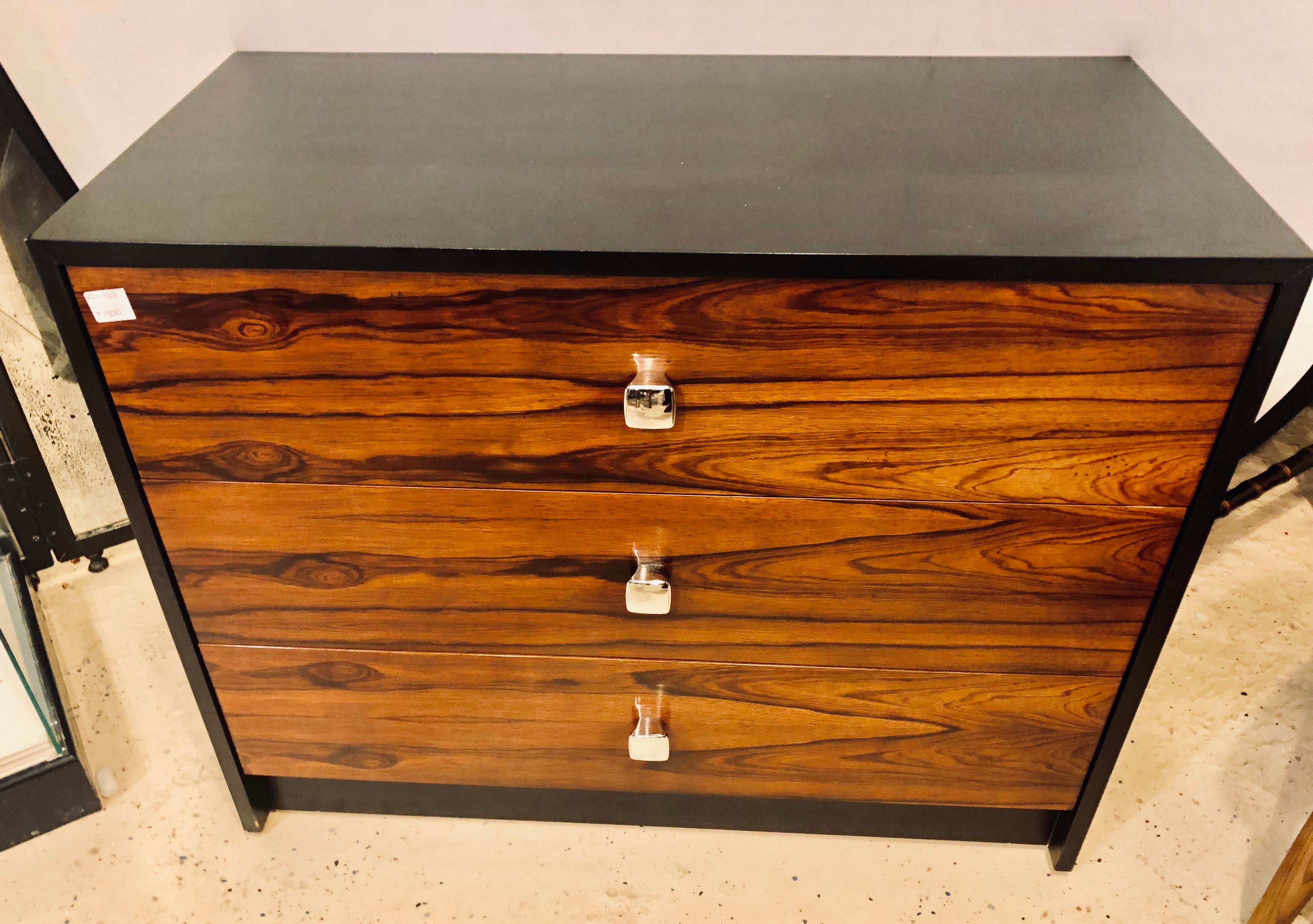 A Mid-Century Modern rosewood and ebony commode / chest or nightstand in the manner of Milo Baughman. This finely polished and decorative chest has an ebony case and rosewood front with chrome drawer pulls. Three large easy opening drawers make this